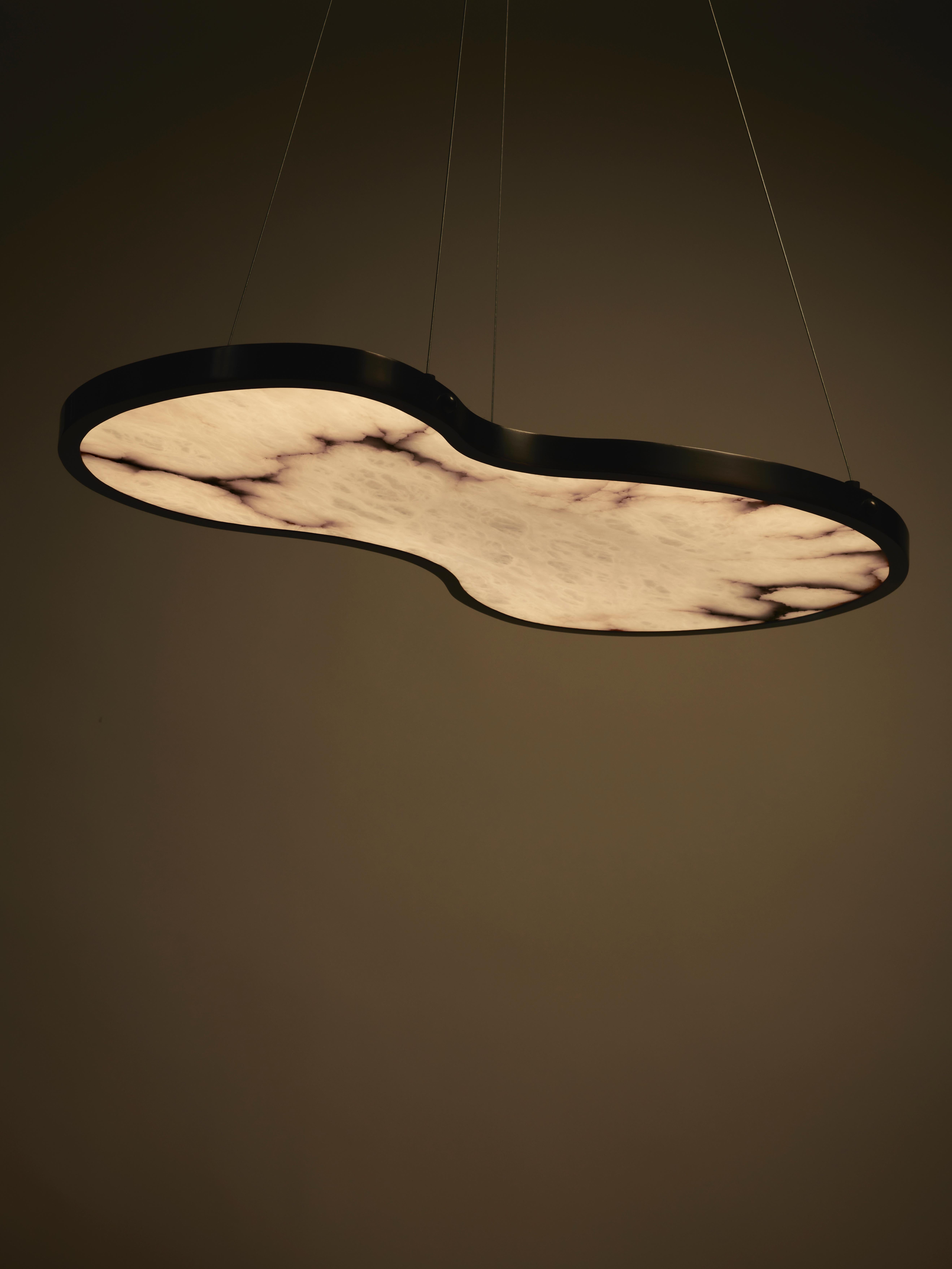 Fabula is a sculptural suspension light with a fluid, organic silhouette where stone transforms into light. A precious backlit alabaster slab, set within a satin bronze frame, creates a refined balance between substance and lightness. The natural