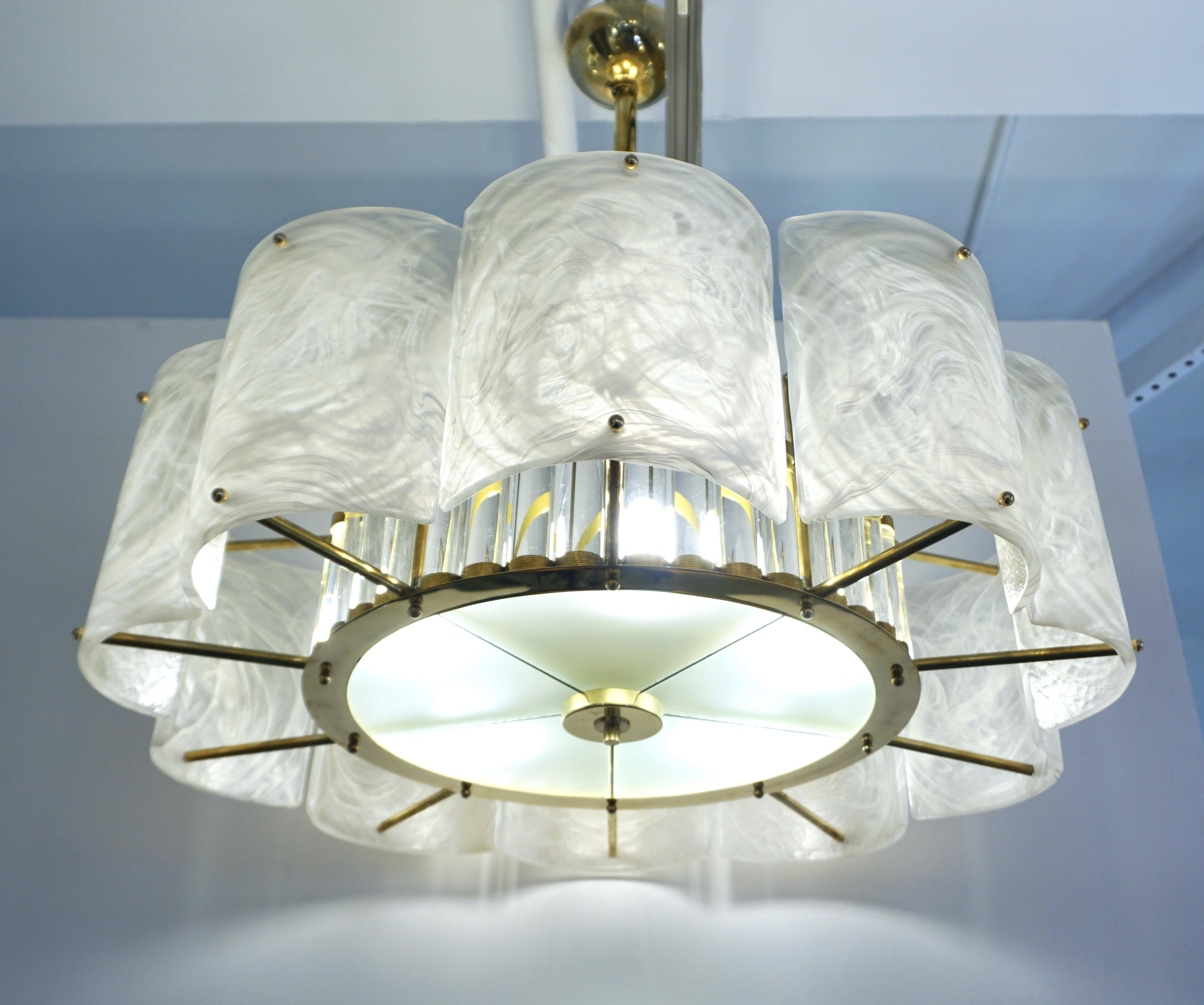 Un lustre moderne innovant et personnalisé, entièrement fabriqué à la main en Italie, avec un double cadre en laiton fait main et un style Hollywood Regency.
L'extérieur est formé d'éléments courbes, comme des voiles, dans un verre Murano innovant