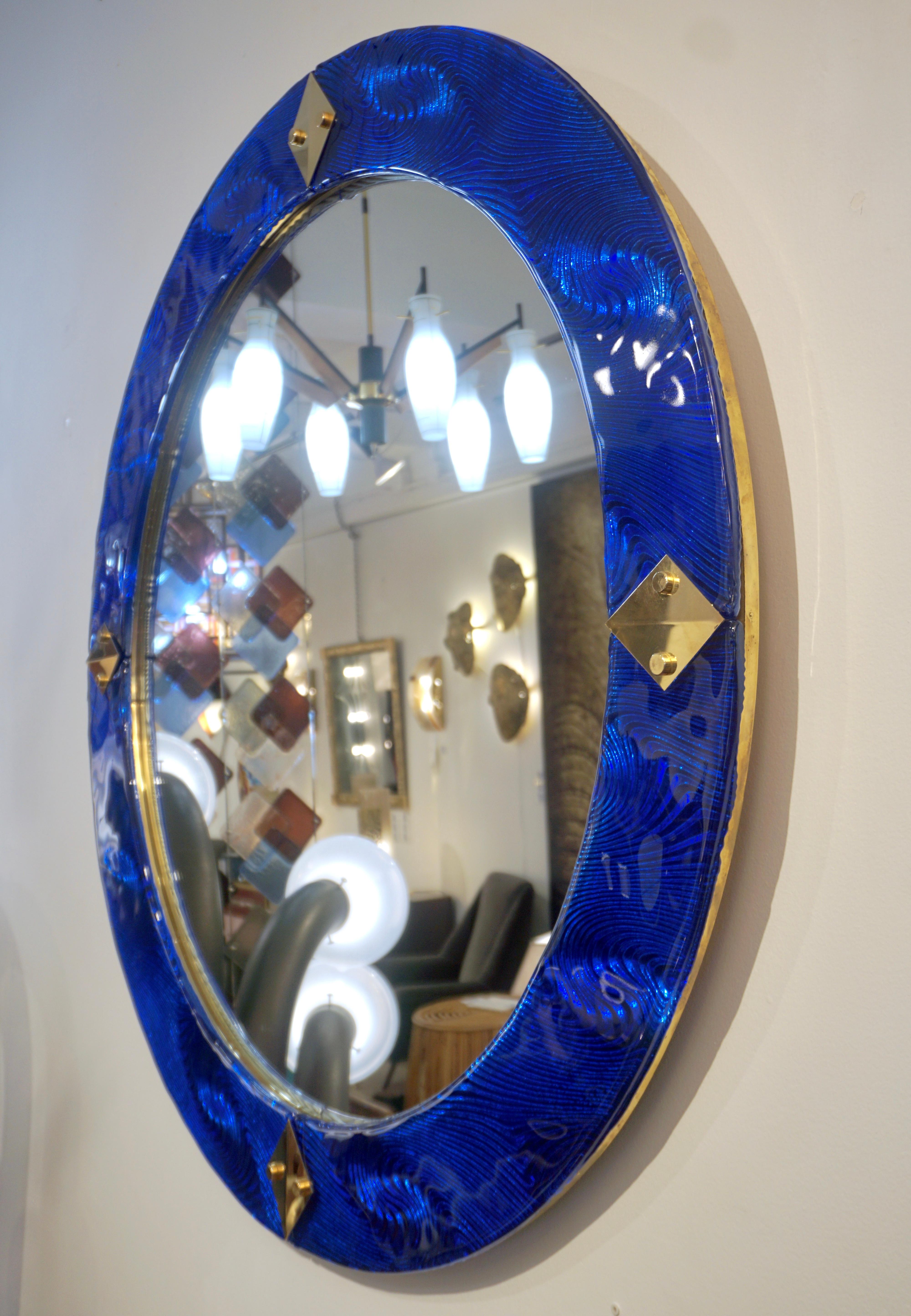 Venetian contemporary round wall mirror, custom made in Italy, framed with a thick border in high quality blown Murano Art glass in a vibrant royal blue sapphire color, artistically rounded at the edge and textured on the reverse with a unique waved