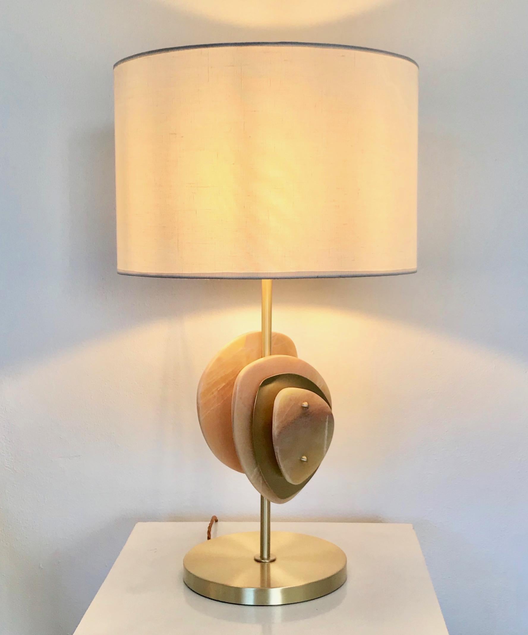 Italian contemporary honey onyx and satin brass table lamp called Satellite, entirely handcrafted in Italy. This organic modern design is inspired by nature, earth and water, with a combination of hand cut flat curved elements in stone and brass