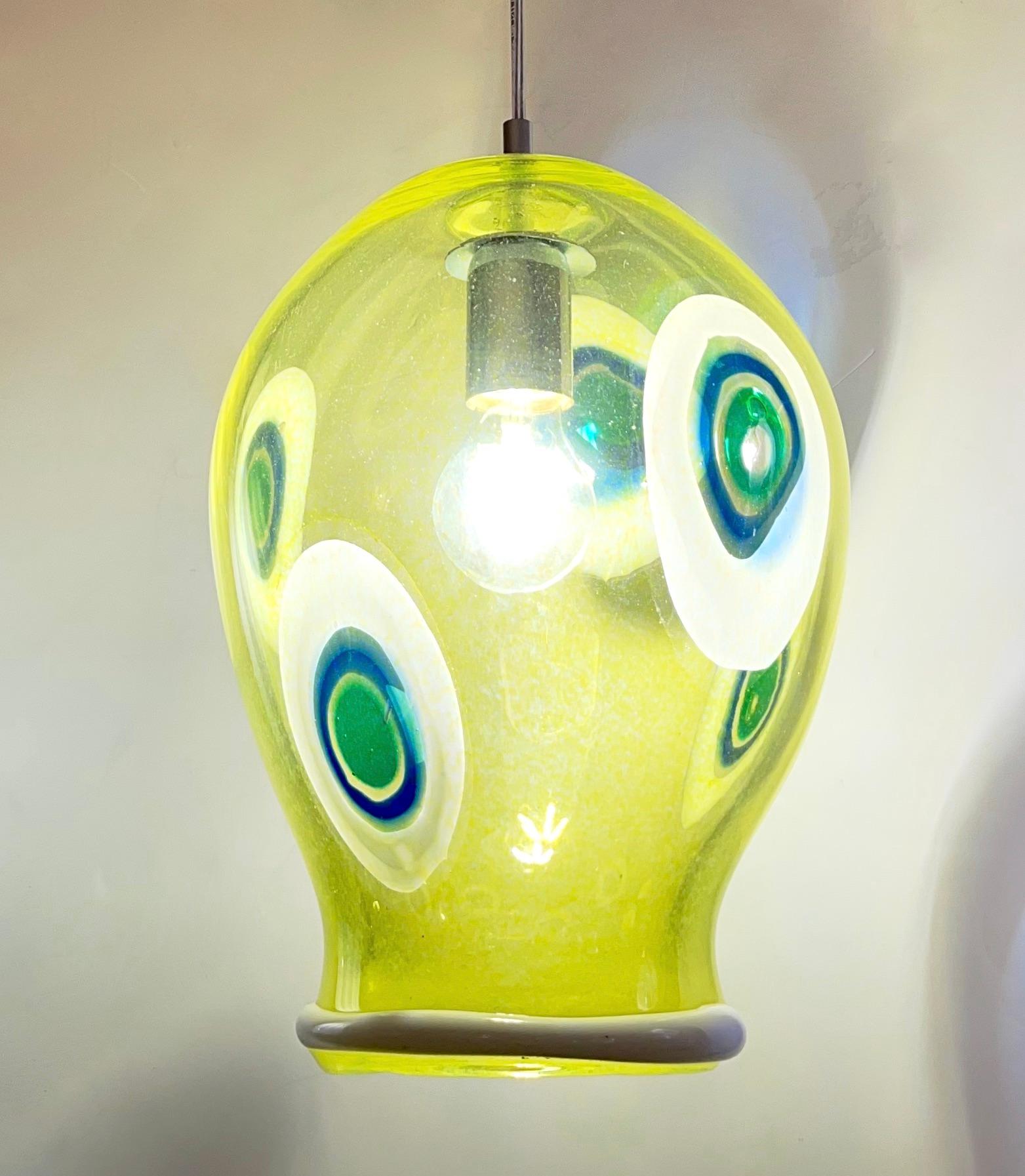 Fun and elegant Italian contemporary custom-made pendant chandelier, of organic modern design, entirely handcrafted with adjustable height, consisting of a sexy curved shade in translucent yellow lime blown Murano glass decorated with white, blu,