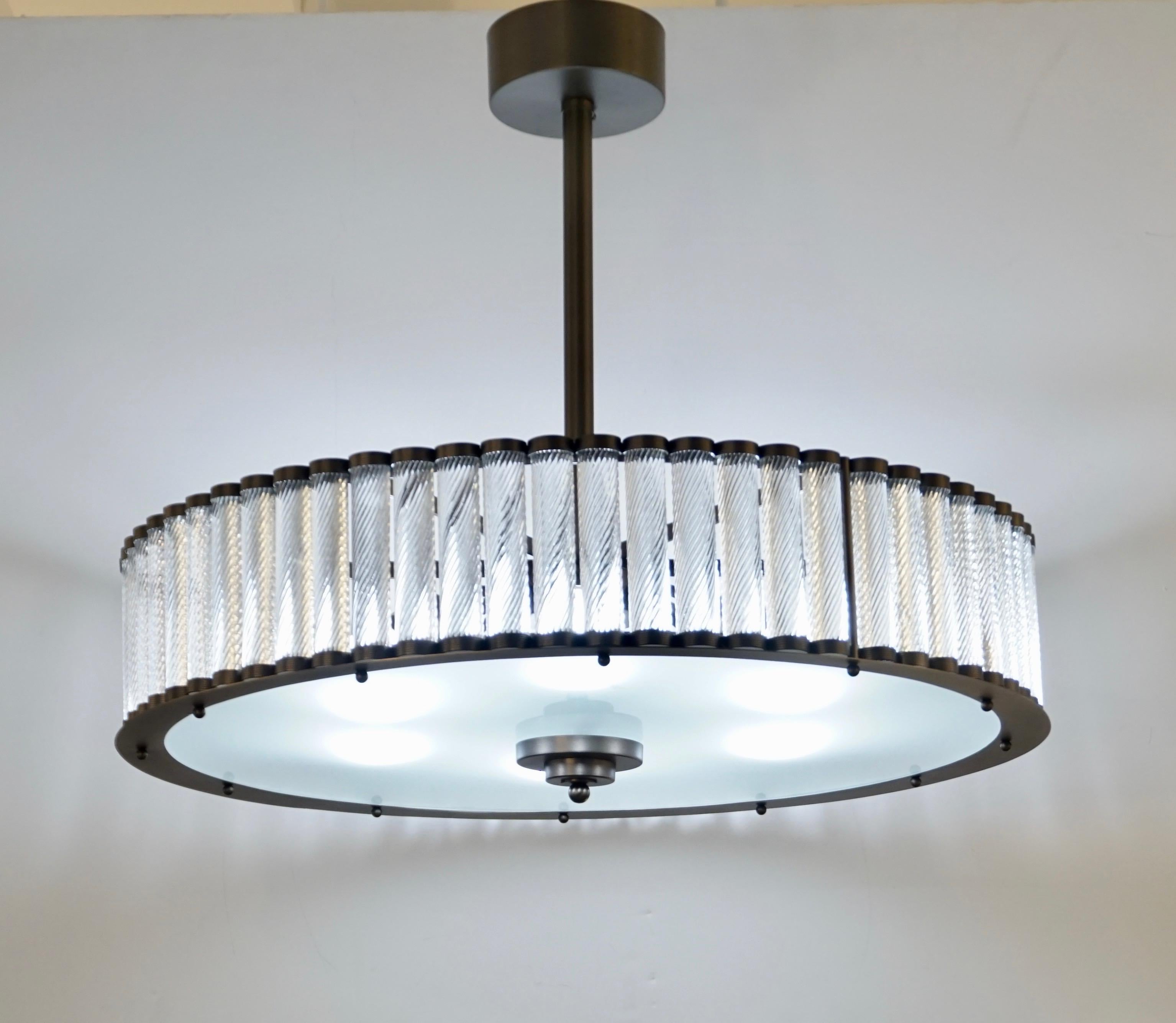 Lampadario/pendente rotondo a forma di tamburo dal design Art Deco italiano contemporaneo e personalizzabile, interamente realizzato a mano, con finitura in acciaio scuro. La struttura in ottone ben smerlata sostiene bacchette in vetro di Murano