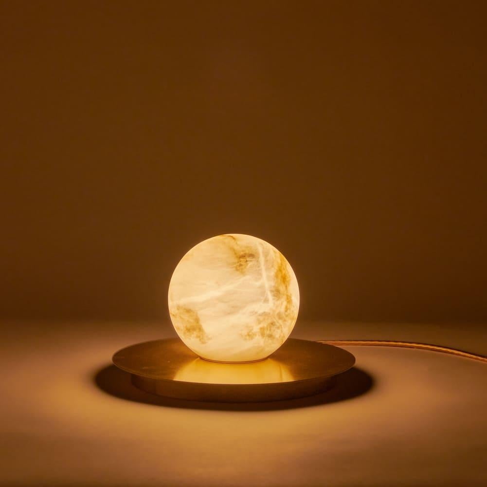 Les propriétés naturelles de l'albâtre en tant que diffuseur : la couleur chaude et la texture de ses veines toujours différentes les unes des autres, rappelant l'atmosphère magique des nuits de pleine lune. Le disque en laiton complète la forme et