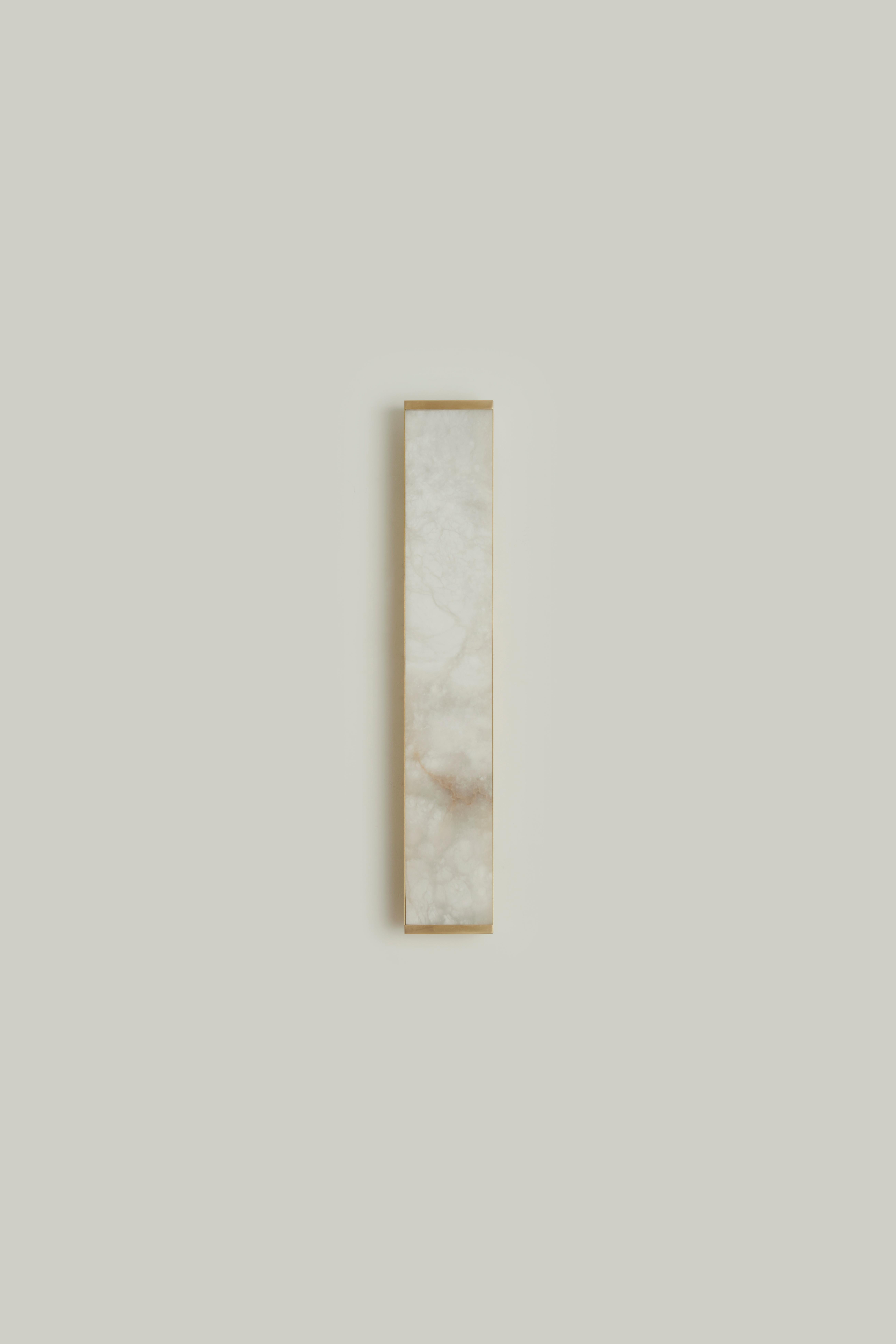 The Tech media wall sconce was conceived with the idea of merging the luminaire with the lampshade into a single element, playing on the transparencies of the light through the ultra-thin onyx encased in a satin brass frame with a simple linear