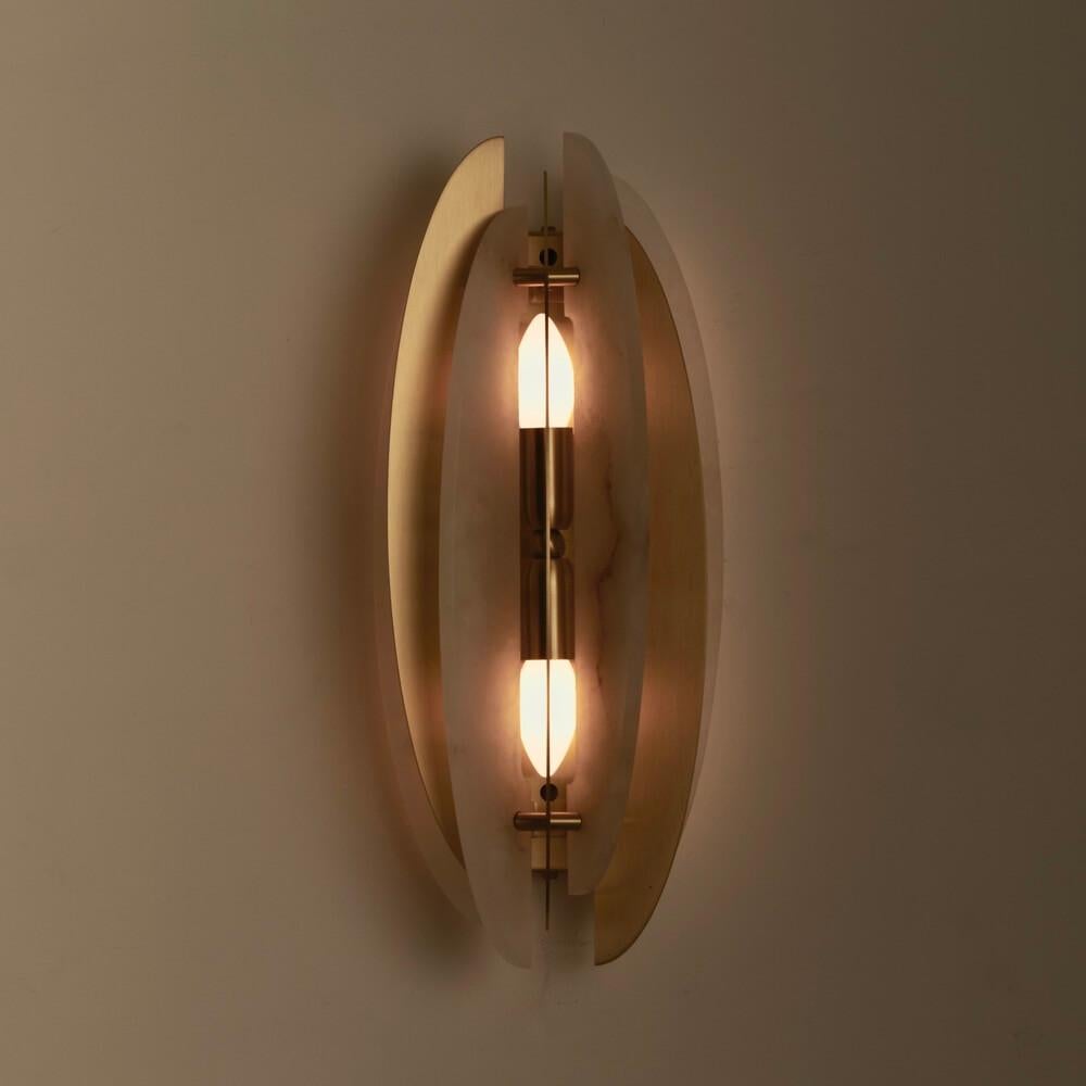 A rhythmic composition of satin brass and natural alabaster blades gives life to a sculptural and luminous wall sconce. Helios stands out for its three-dimensional elliptical design, where metal and stone elements alternate in perfect formal