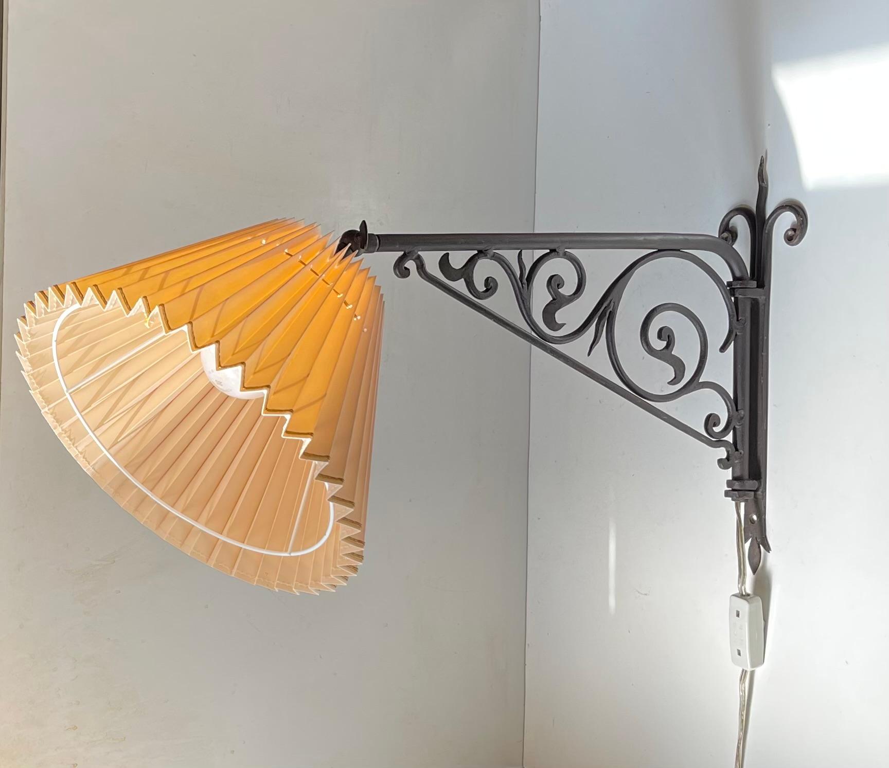 A 180 degree adjustable swing arm wall lamp made from ornamental hand-welded wrought iron. It also adjustable by the shade and features a period face-powder colored fluted shade with textile gold bands. It was made in Italy during the late 1940s in