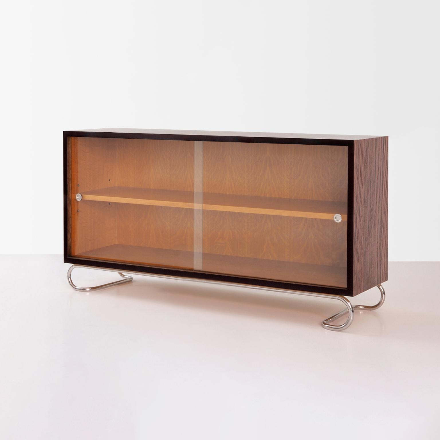 Librería baja a medida con caja de tablero de madera chapada y paneles de cristal deslizantes y base de acero tubular.
