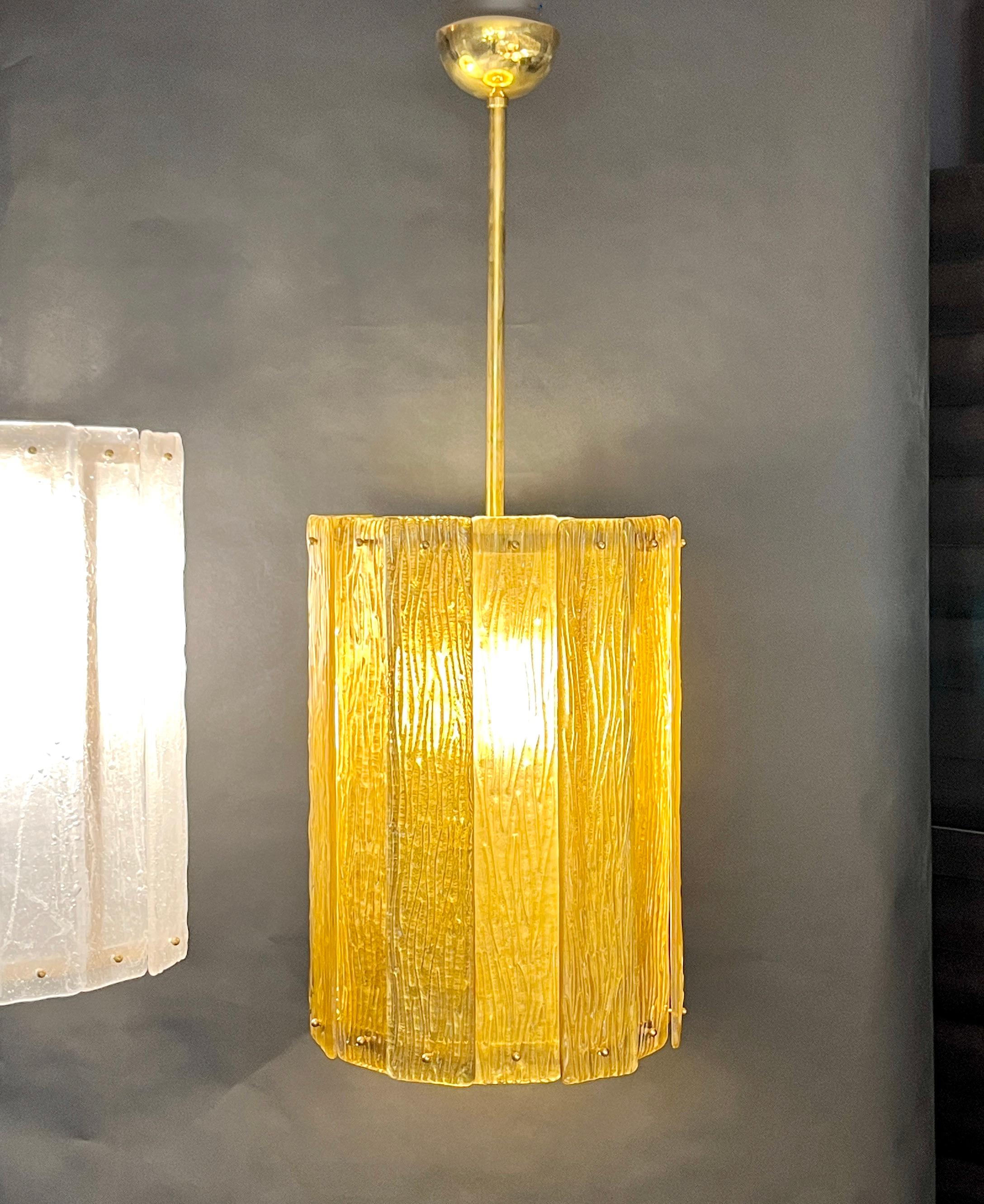 Unique contemporary Italian Art Deco design round pendant chandelier, entirely handcrafted. This light fixture is composed of a handmade brass structure supporting gold textured overlapping Murano glass bands, the amber glass decorated on reverse
