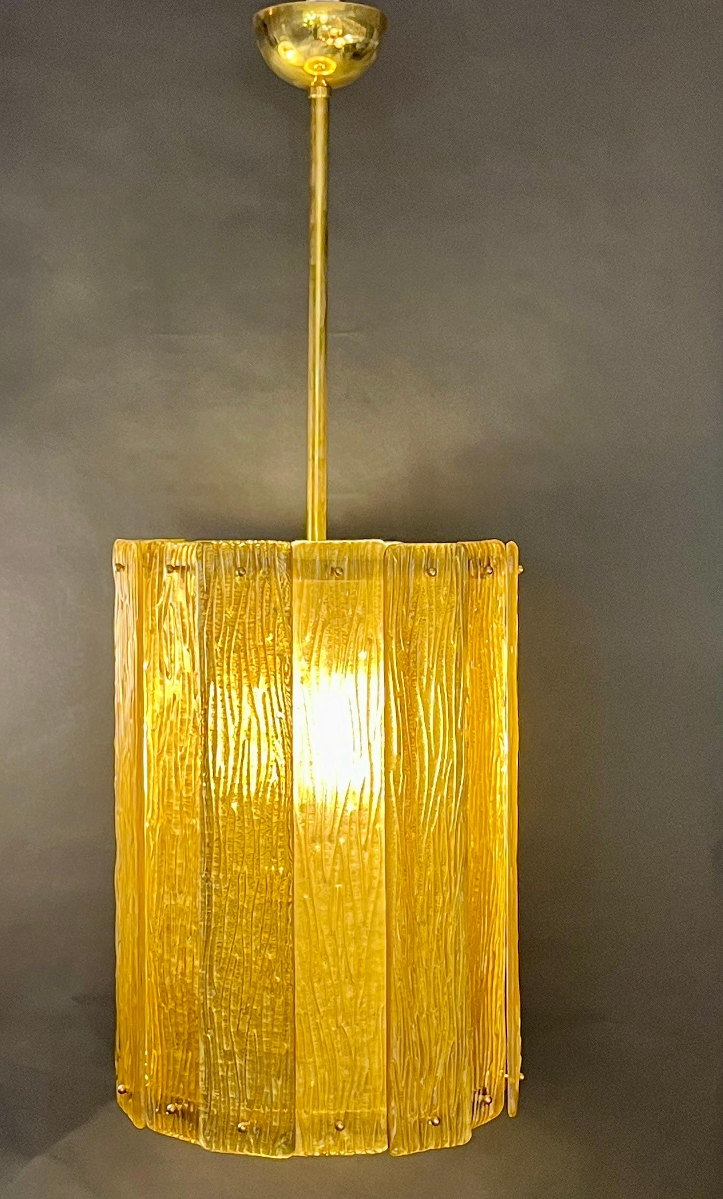 Unique contemporary Italian Art Deco design round pendant chandelier, entirely handcrafted. This light fixture is composed of a handmade brass structure supporting gold textured overlapping Murano glass bands, the amber glass decorated on reverse