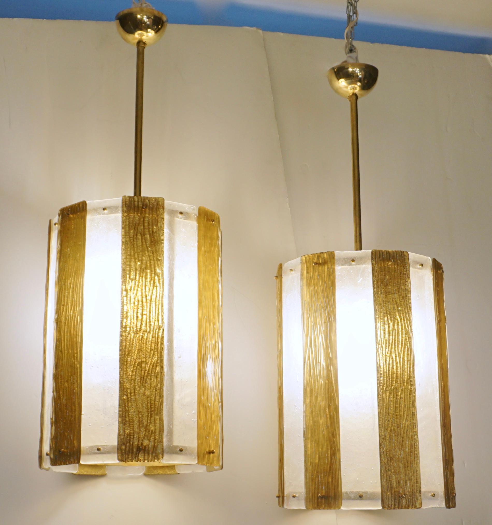 A pair is available - Unique contemporary Italian Art Deco design round pendant chandelier, entirely handcrafted. This light fixture is composed of a handmade brass structure supporting alternating textured Murano glass bands, the frosted crystal