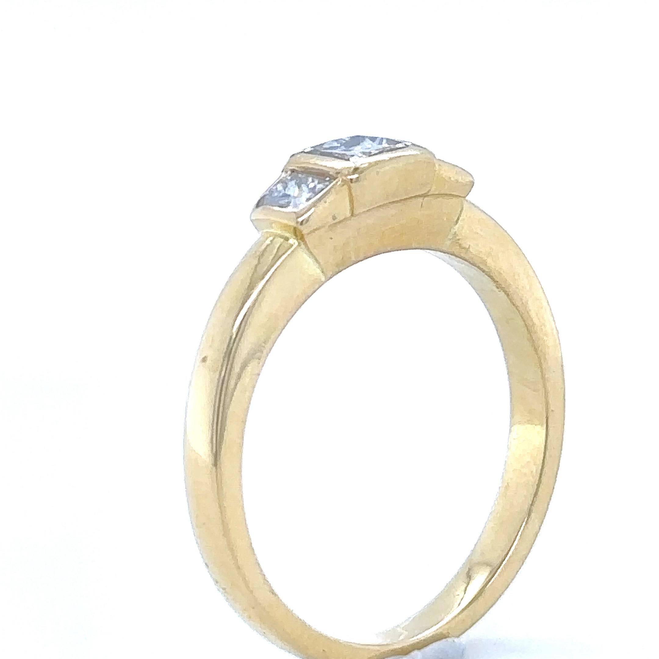 A Princess Cut Diamond Ring, bezel set in 18ct yellow gold with a princess cut diamond on each shoulder on a 2.4mm band.

Diamonds 1 = 0.40ct (estimated), Graded in setting as Colour: G to H, Clarity: VS

Diamonds 2 = 0.30ct (estimated), Graded in