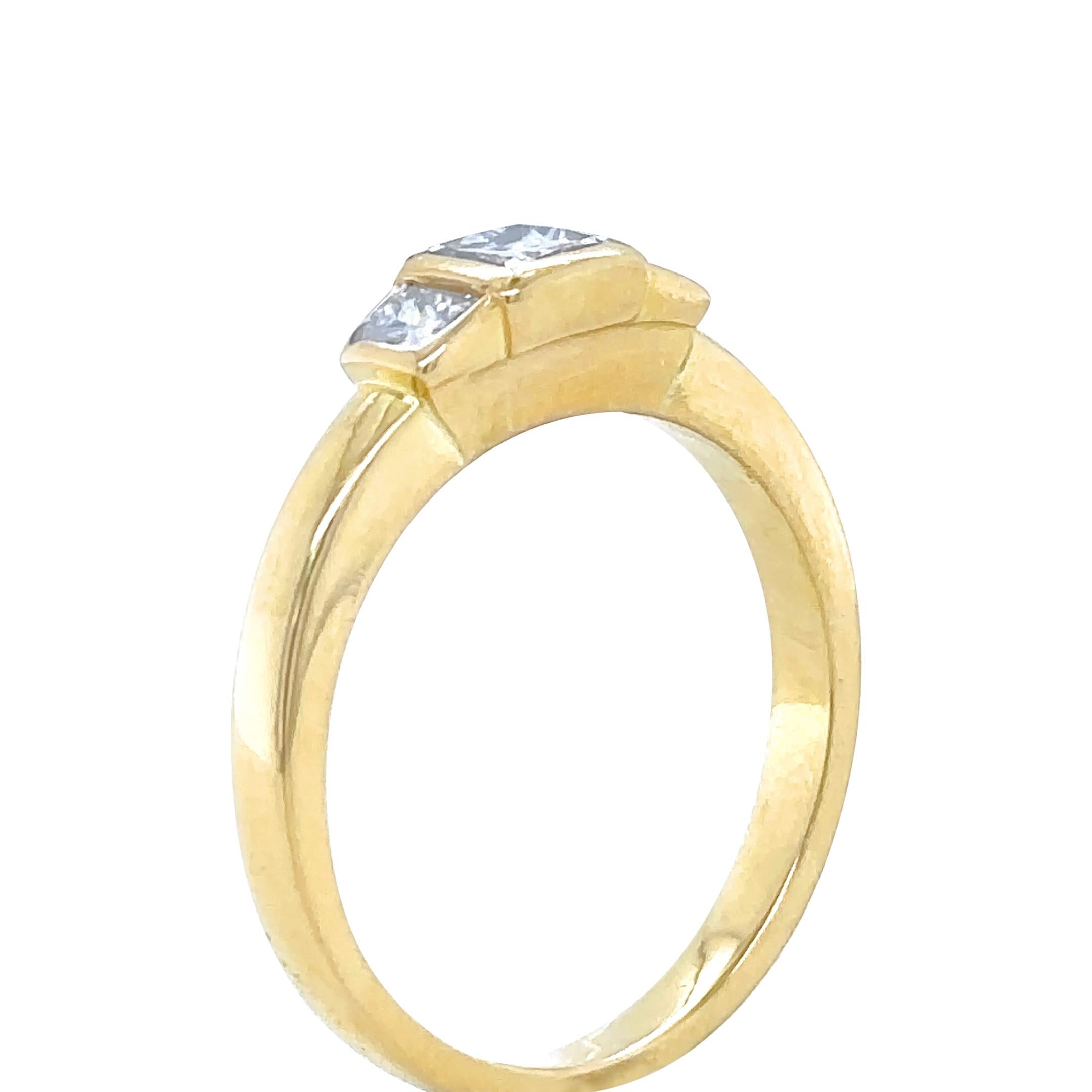A Princess Cut Diamond Ring, bezel set in 18ct yellow gold with a princess cut diamond on each shoulder on a 2.4mm band.

Diamonds 1 = 0.40ct (estimated), Graded in setting as Colour: G to H, Clarity: VS

Diamonds 2 = 0.30ct (estimated), Graded in