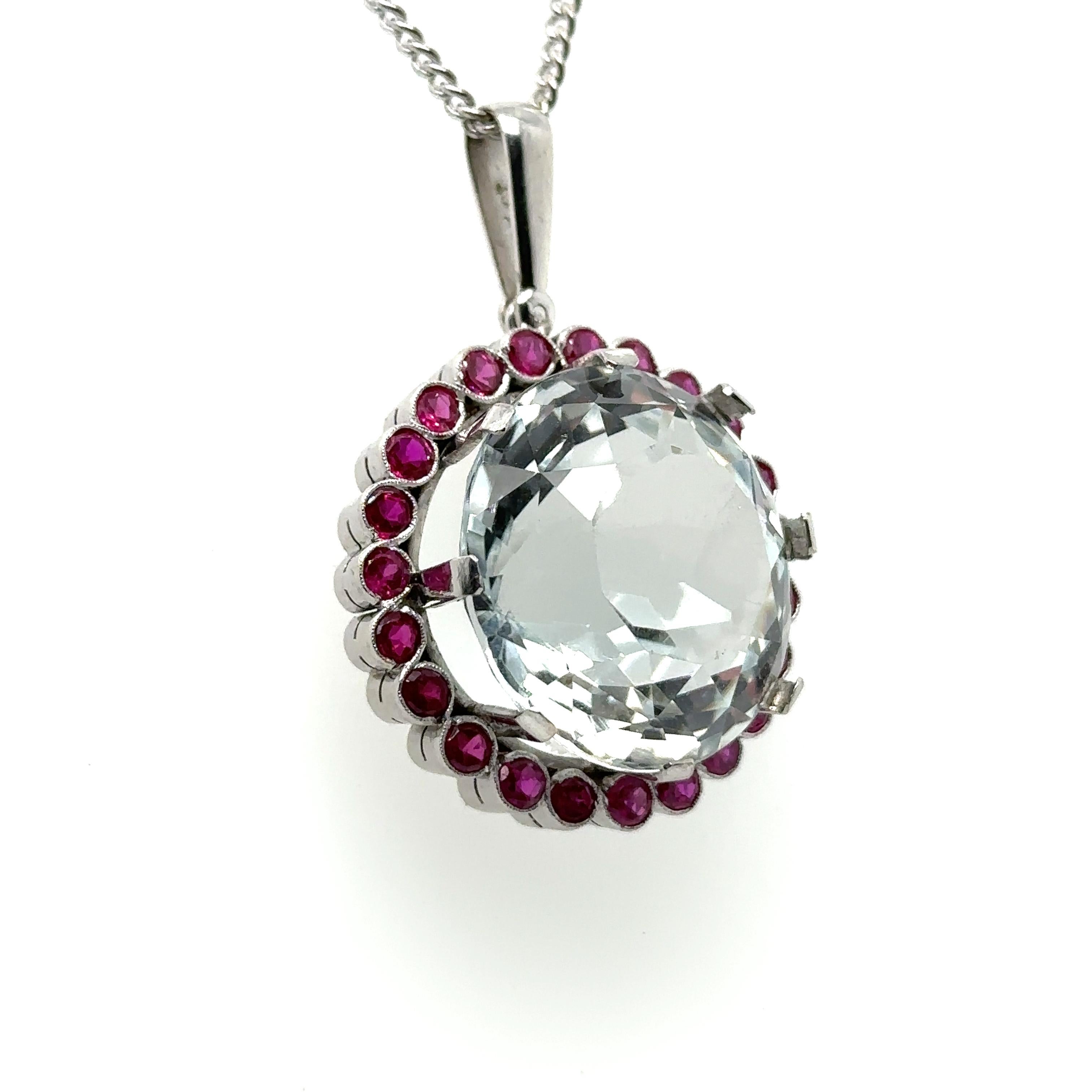 A Round Rock Crystal Round Cluster Pendant, claw set in 18ct white gold within a border of 23 round synthetic rubies.

Rock Crystal 30.00ct (estimated), 20.5mm diameter, 14.0mm depth. Synthetic rubies 2.5mm

Handmade mount

Metal: 18ct White