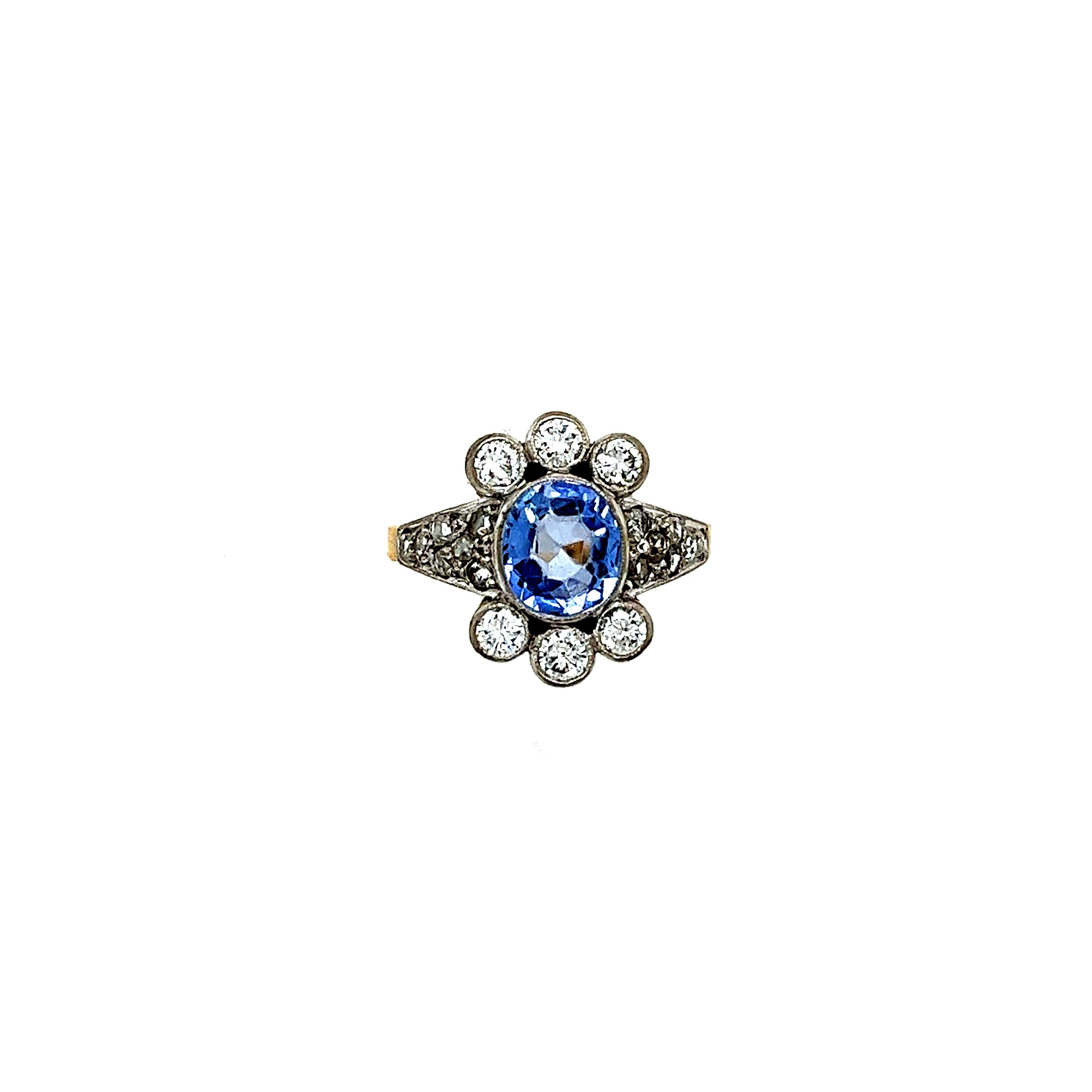 A Sapphire And Diamond Cluster Ring, with an oval Ceylon sapphire bezel set in 18ct white on yellow gold surrounded by 6 round brilliant cut diamonds and with 14 rose cut diamonds pavé set on the shoulders on a 2.2mm band.

Sapphire 1.80ct