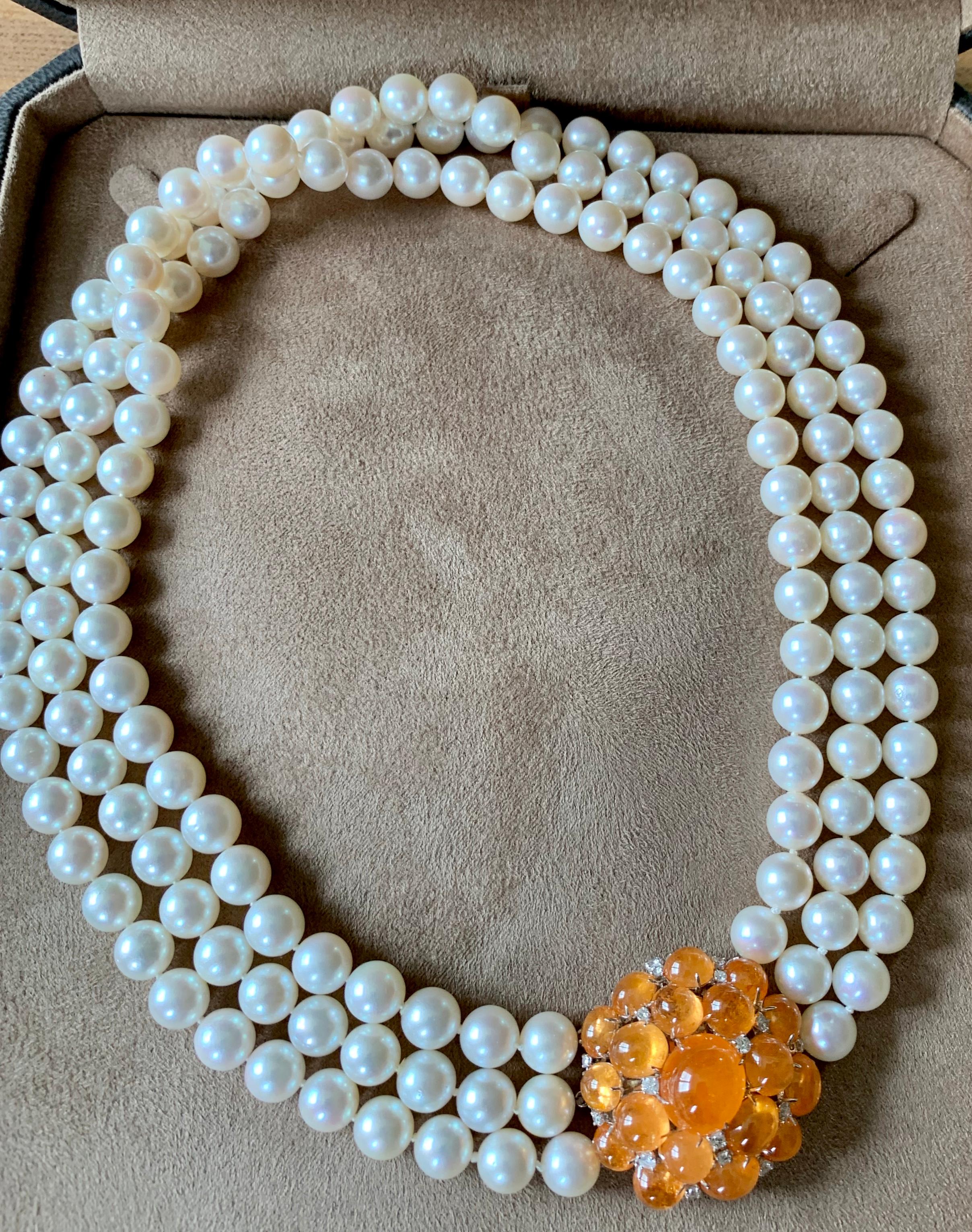 Elegant three row Akoya pearl with an eye catching clasp that consists of vivid orangey Mandarin Garnet Cabochons that are accentuated by small brilliant cut Diamonds. 
Pearls are high quality, the best lustre and free from blemishes as you can see