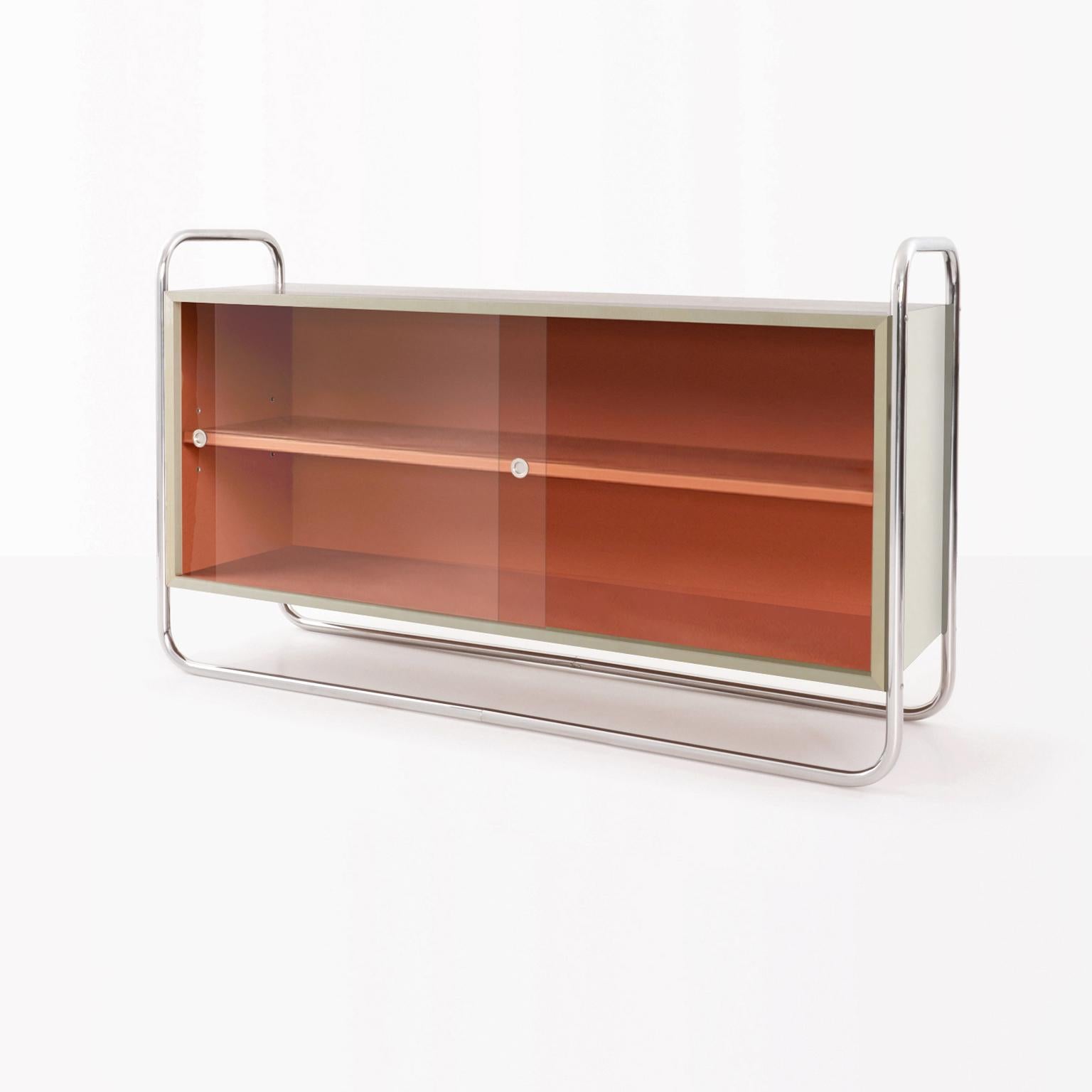 Bauhaus tubular steel low bookcase with case in chrome plated metal, lacquered blockboard and sliding glass panels. 
