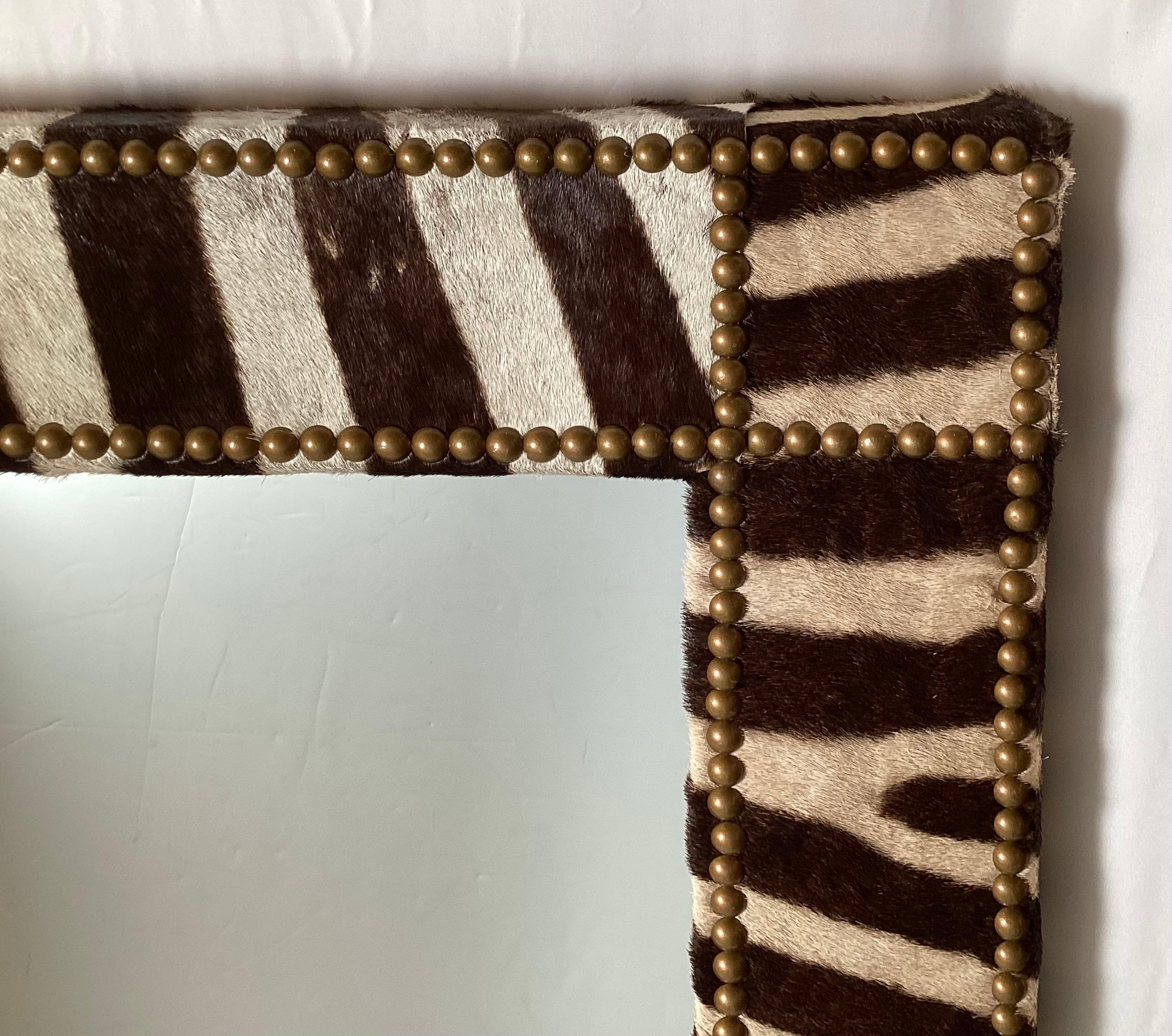 A very chic custom Zebra hide framed mirror.  The solid wood frame, covered in zebra with antiqued brass nail head trim.  The framed mirror measures 65 inches high, 34 inches wide. 
