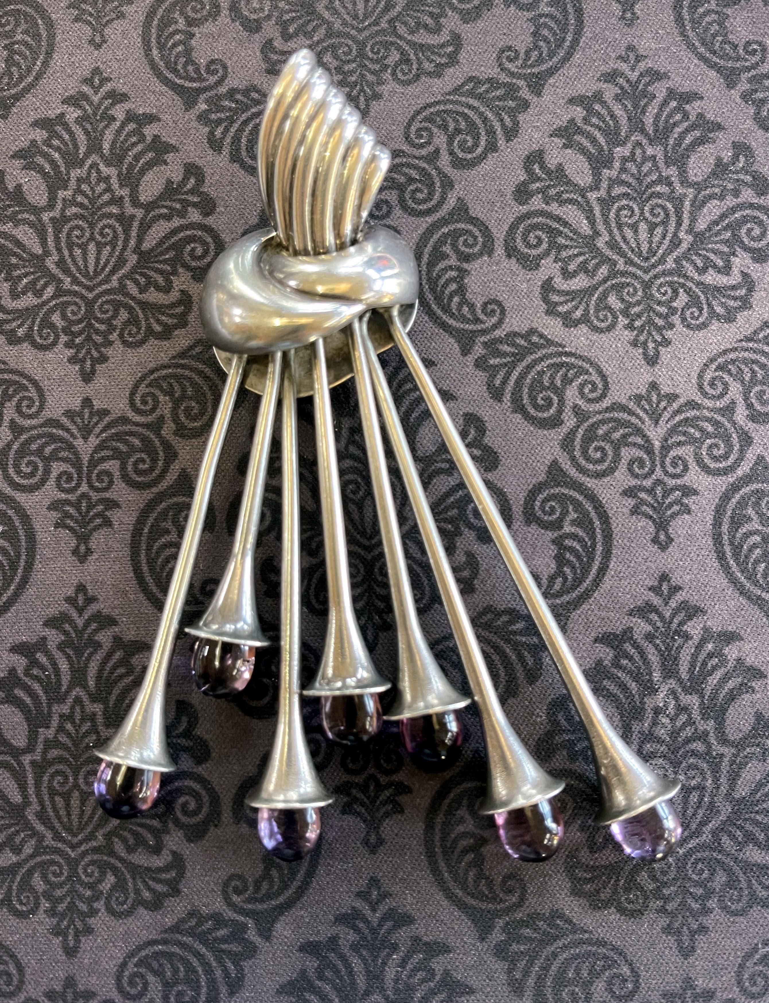 A large Mexican Modern brooch by Antonio Pineda Taxco circa 1950-60s. The bespoken piece features seven articulated sprays from a ribbon knot, stamens-like, and capped with amethyst stones at the ends. The design is bold and refined at the same