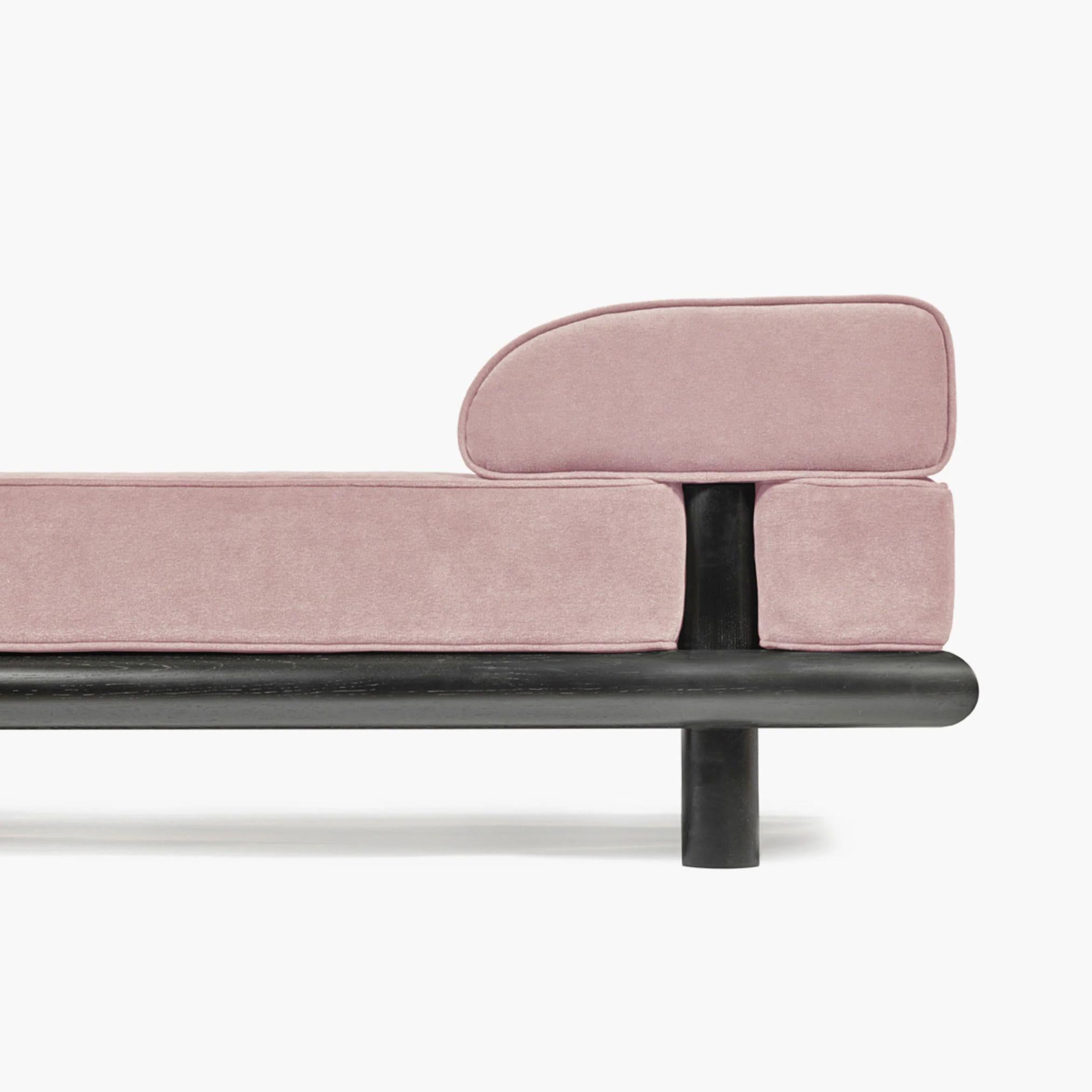 Beth est une pièce polyvalente conçue par Ann Demeulemeester qui fait office de canapé, de banc ou de lit de jour d'une longueur généreuse de 280 centimètres. Ses profils aux bords arrondis et son cadre en chêne teinté en noir reflètent une approche