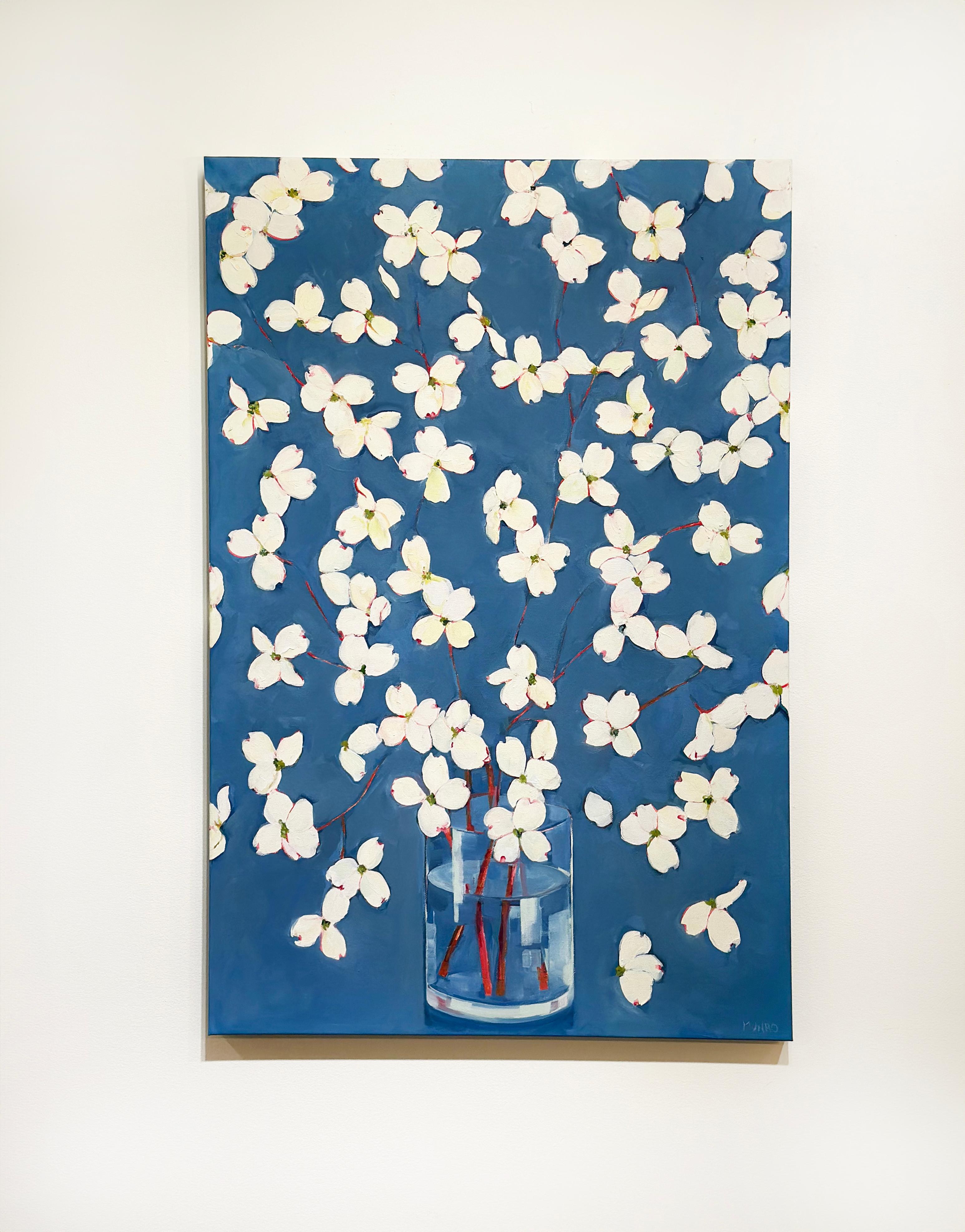 Cette peinture florale contemporaine présente une composition élégante de délicates fleurs blanches gracieusement disposées dans un vase en verre transparent sur un fond bleu riche et vibrant. Évoquant la fraîcheur du printemps, le tableau est