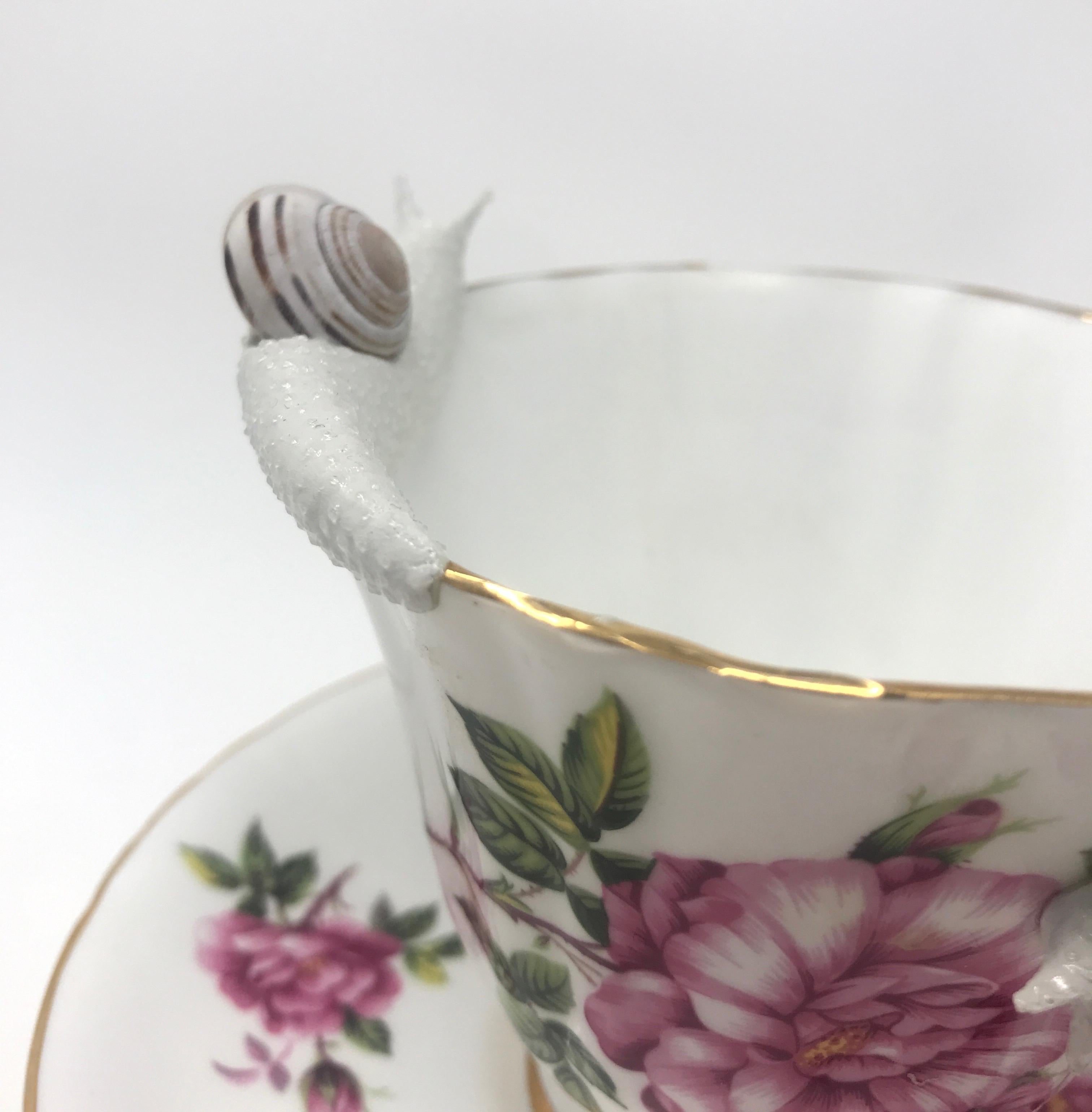 This piece was created with real found snail shells and a durable epoxy clay.  Hand formed by New York artist, Bethany Krull,  the undulating snails circle the delicate rim of this floral teacup.  The glistening wet creatures are surfaced with many