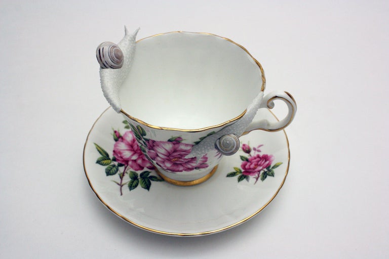 This piece was created with real found snail shells and a durable epoxy clay.  Hand formed by New York artist, Bethany Krull,  the undulating snails circle the delicate rim of this floral teacup.  The glistening wet creatures are surfaced with many