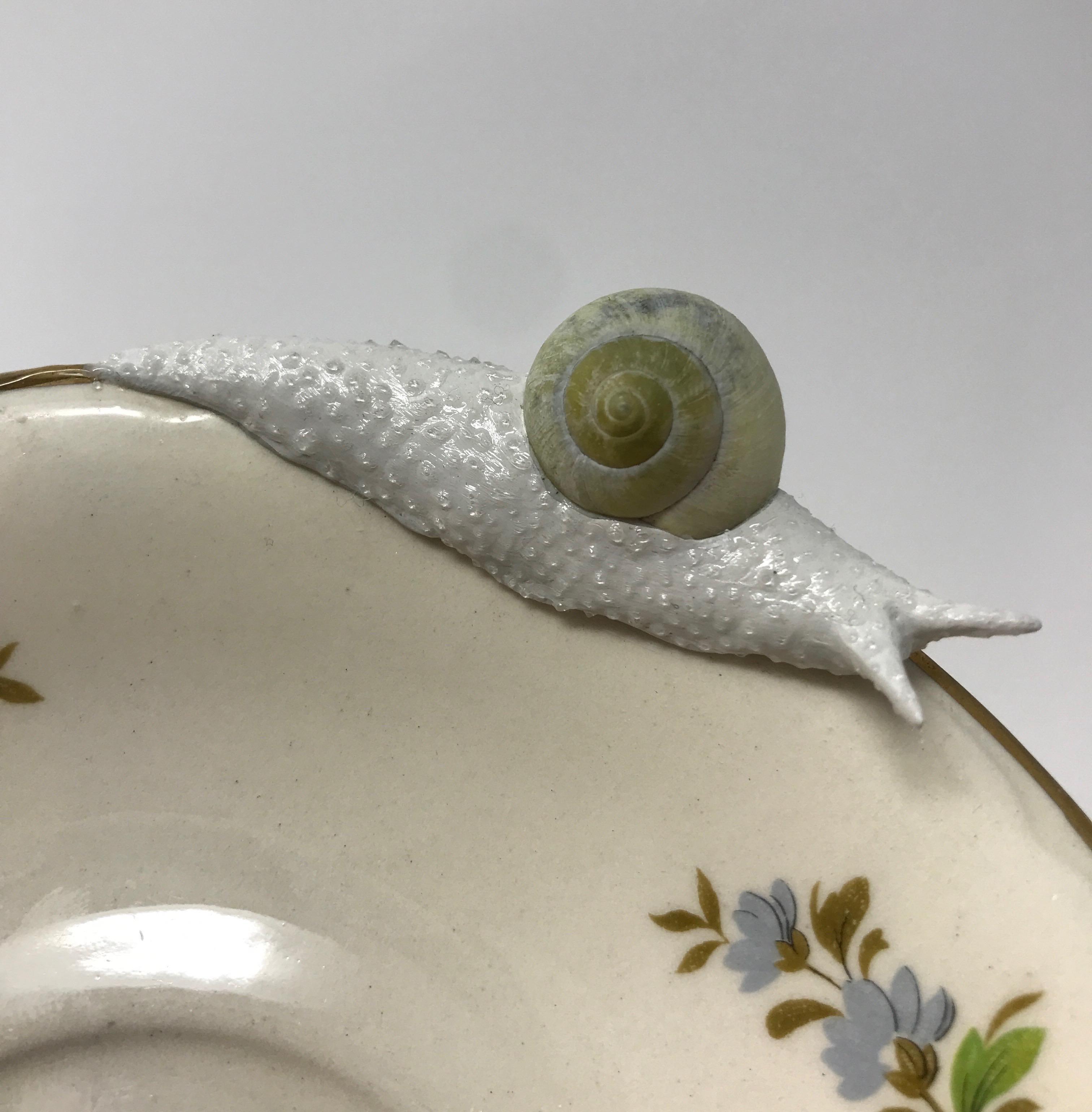 This piece was created with a real found snail shell and durable epoxy clay by New York artist, Bethany Krull to traverse the surface of the floral plate.  The glistening wet snail form is surfaced with many layers of paint before applying the final
