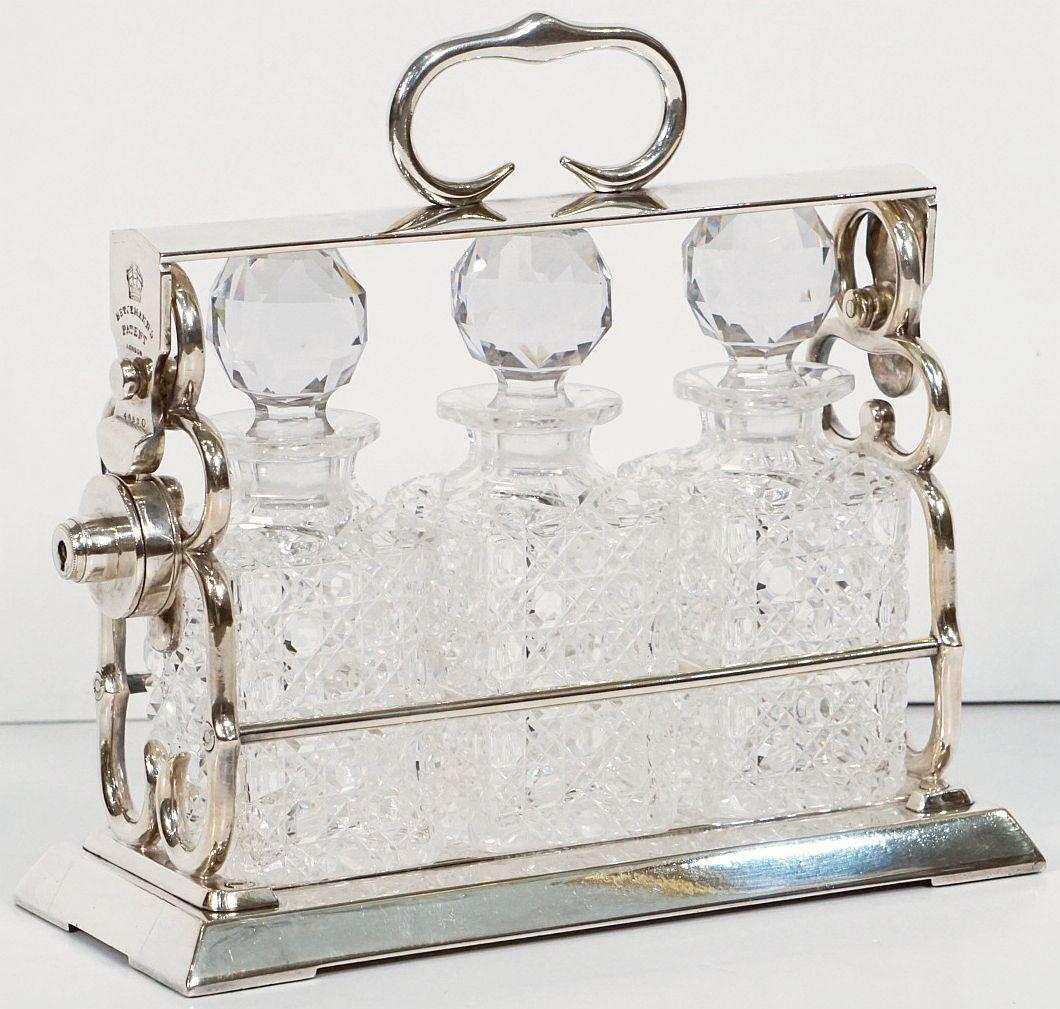 A handsome Betjemann's patent tantalus drinks or spirits three-bottle decanter set of fine plate silver from Edwardian-era England

The tantalus has a silver plated handle and locking mechanism, the hobnail decanters are square in shape and heavily