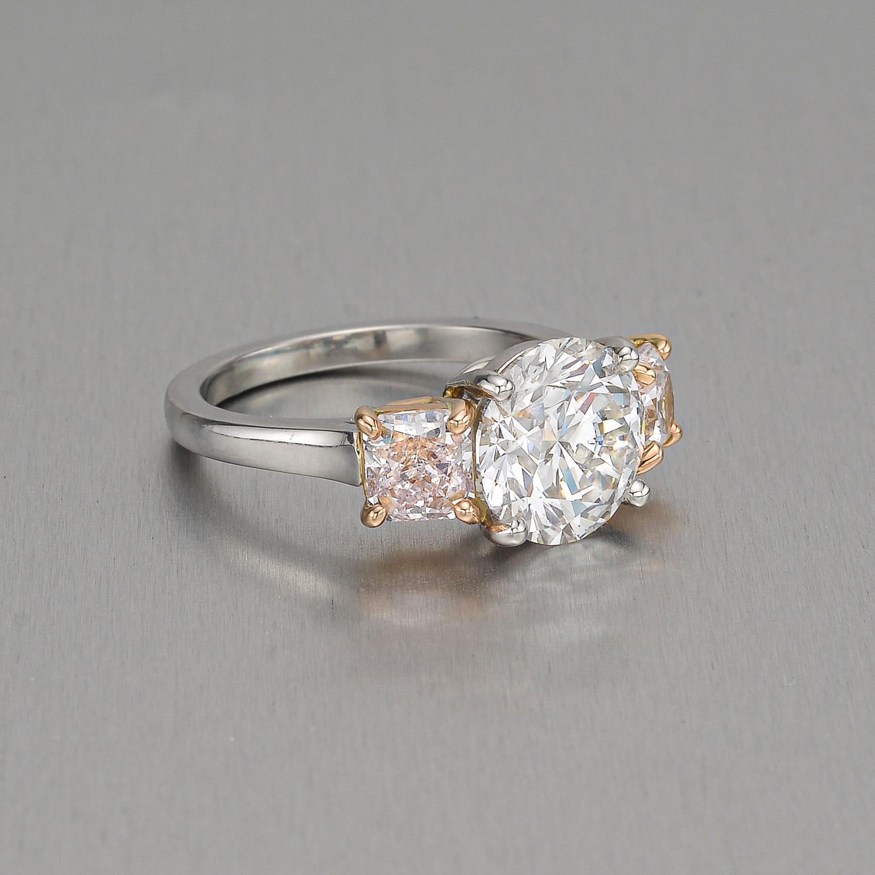 Three-stone engagement ring, centering a fine near-colorless round brilliant-cut diamond weighing 2.51 carats with radiant-cut natural fancy very light pink diamond sides, in a platinum and 18k pink gold mounting.

Two very light pink diamonds