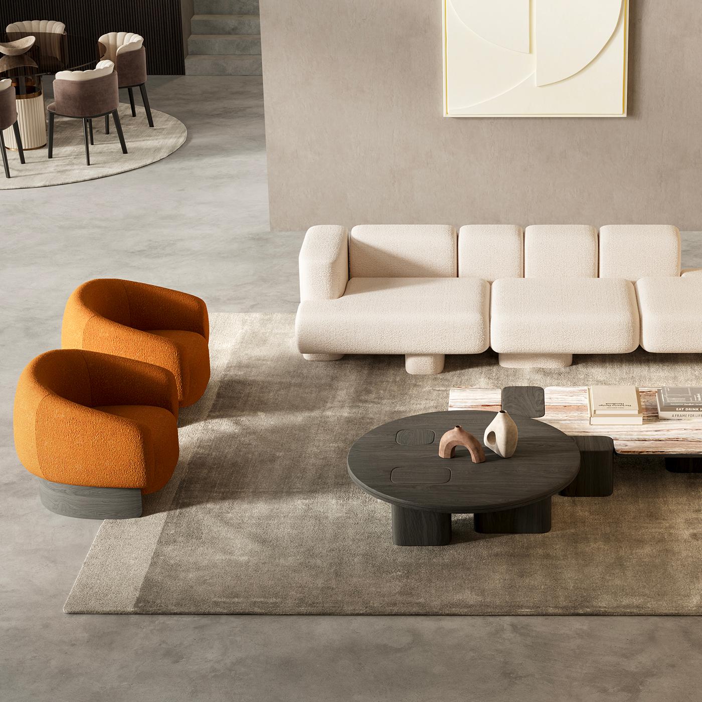 An enveloping comfort characterizes this armchair which has sinuous lines and is supported by a curved ash wood base. The peculiarity is undoubtedly found in the new bouclé fabric with which it is upholstered. Fango finishing. The upholstery is