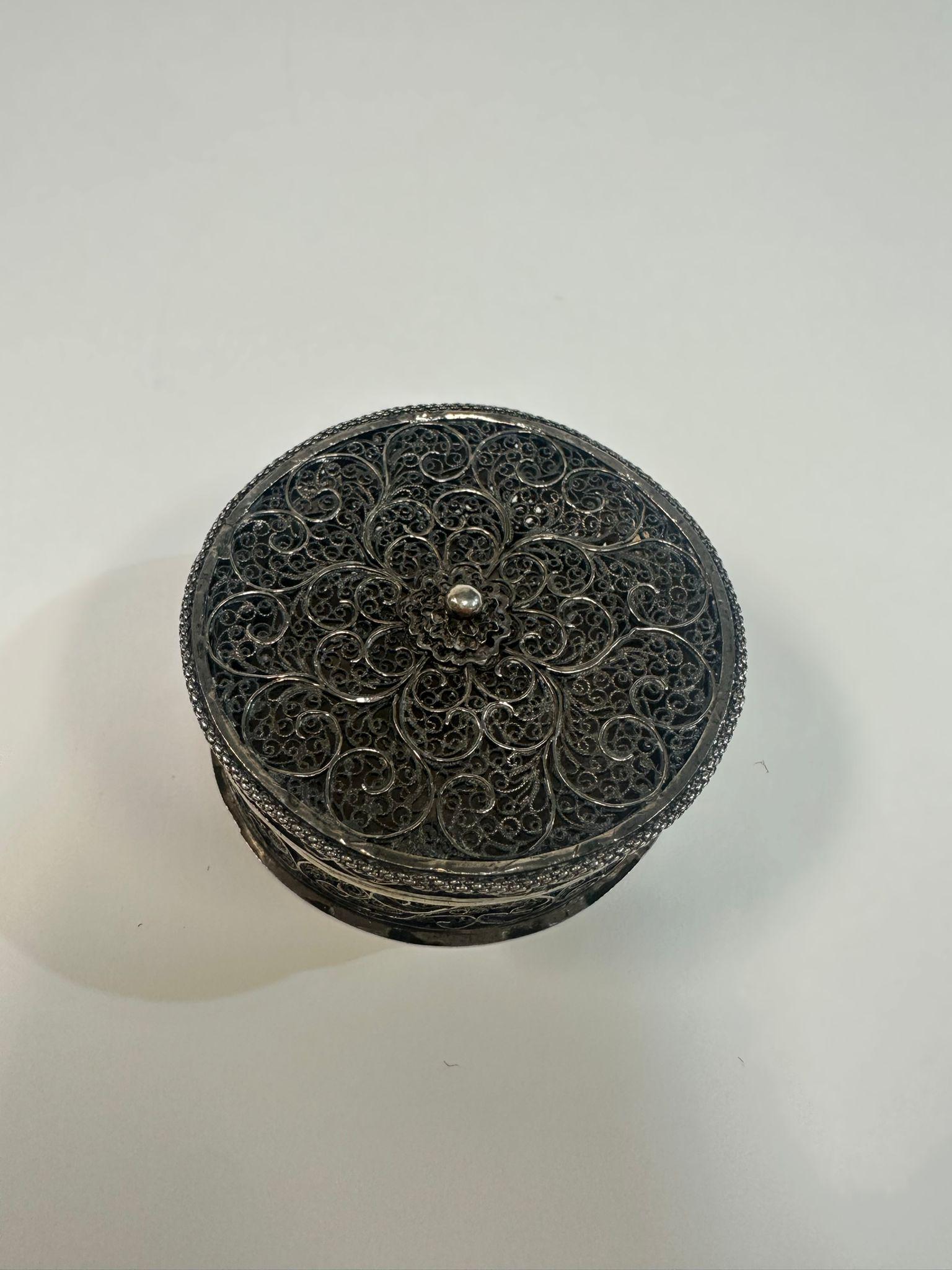This is a meticulously handcrafted silver filigree spice box, created in the Bezalel School of Arts and Crafts tradition, a hallmark of early 20th-century Jewish artistic expression in Jerusalem. The round form is adorned with intricate openwork