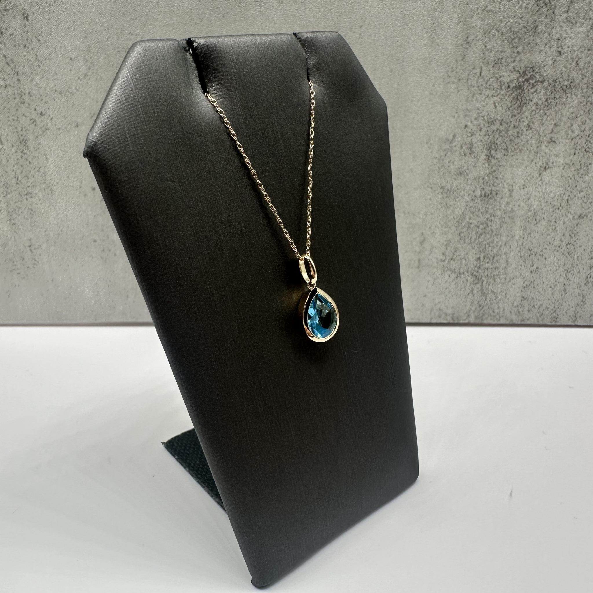 This stunning Bezel Set Blue Topaz Necklace in 14kt yellow gold features an 8x6mm pear-cut blue topaz, showcasing a vibrant and striking blue hue. The 18-inch length fits comfortably around the neck, and the spring ring clasp ensures a secure fit.