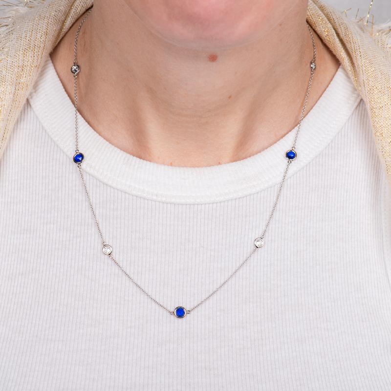 This diamond by the yard style necklace features bezel set bright blue round spinels alternating with natural round bezel set diamonds set in 14 karat white gold. Lobster clasp closure. The length is 18