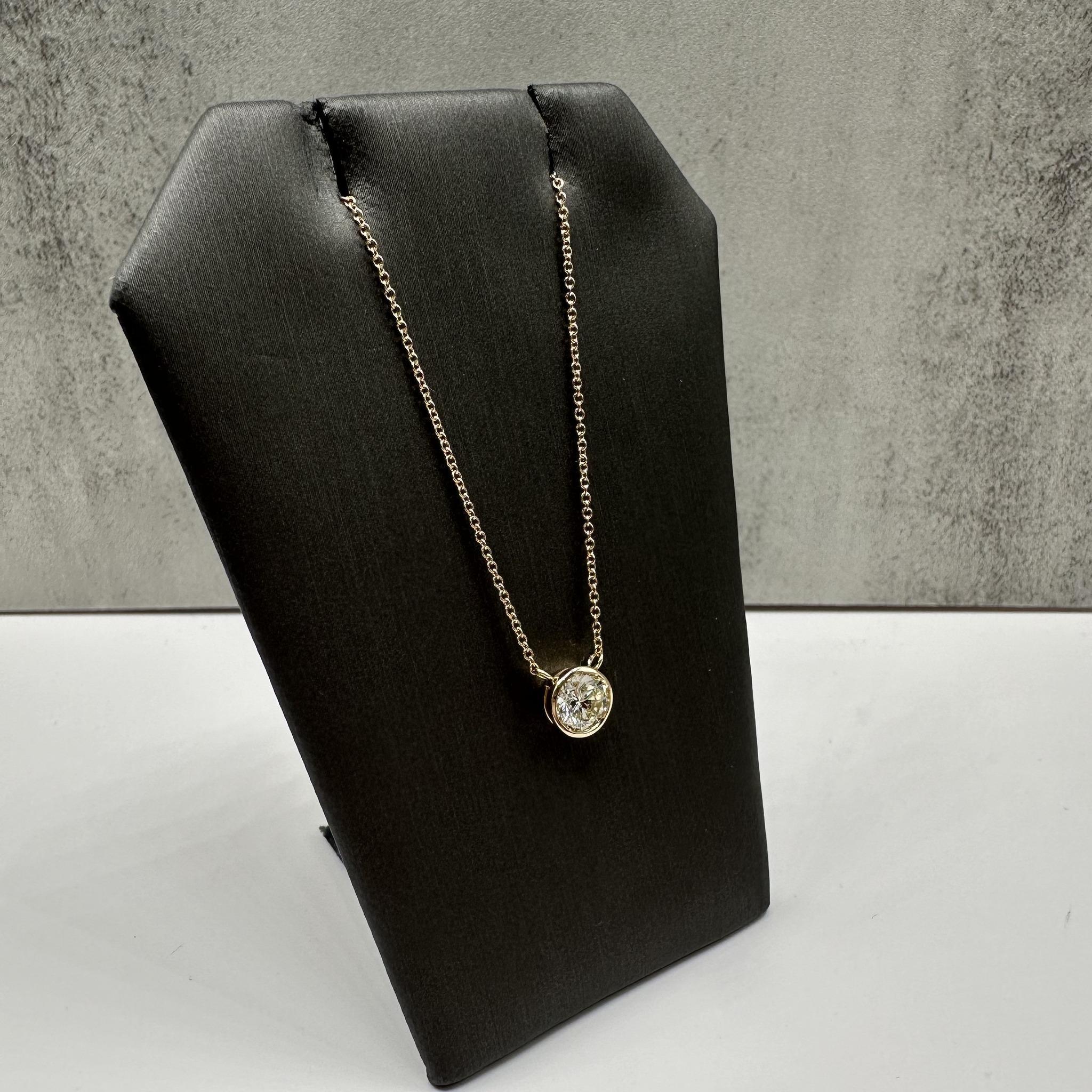 This stunning Bezel Set Diamond Necklace in 14kt yellow gold features a 0.74ct natural N, SI1 round diamond, GIA certified for authenticity and quality. The diamond faces up beautifully in the bezel, showcasing its brilliance. Weighing 2 grams, the