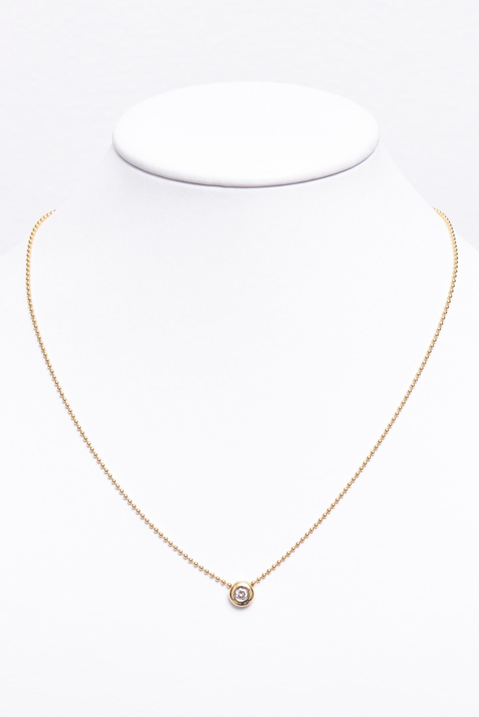 Pendentif italien en diamant de très belle facture présentant un diamant rond d'environ 0,20 carat serti dans un chaton en or jaune 18 carats.  Le diamant est percé de part et d'autre pour pouvoir être glissé sur la chaîne à boules.  La chaîne est