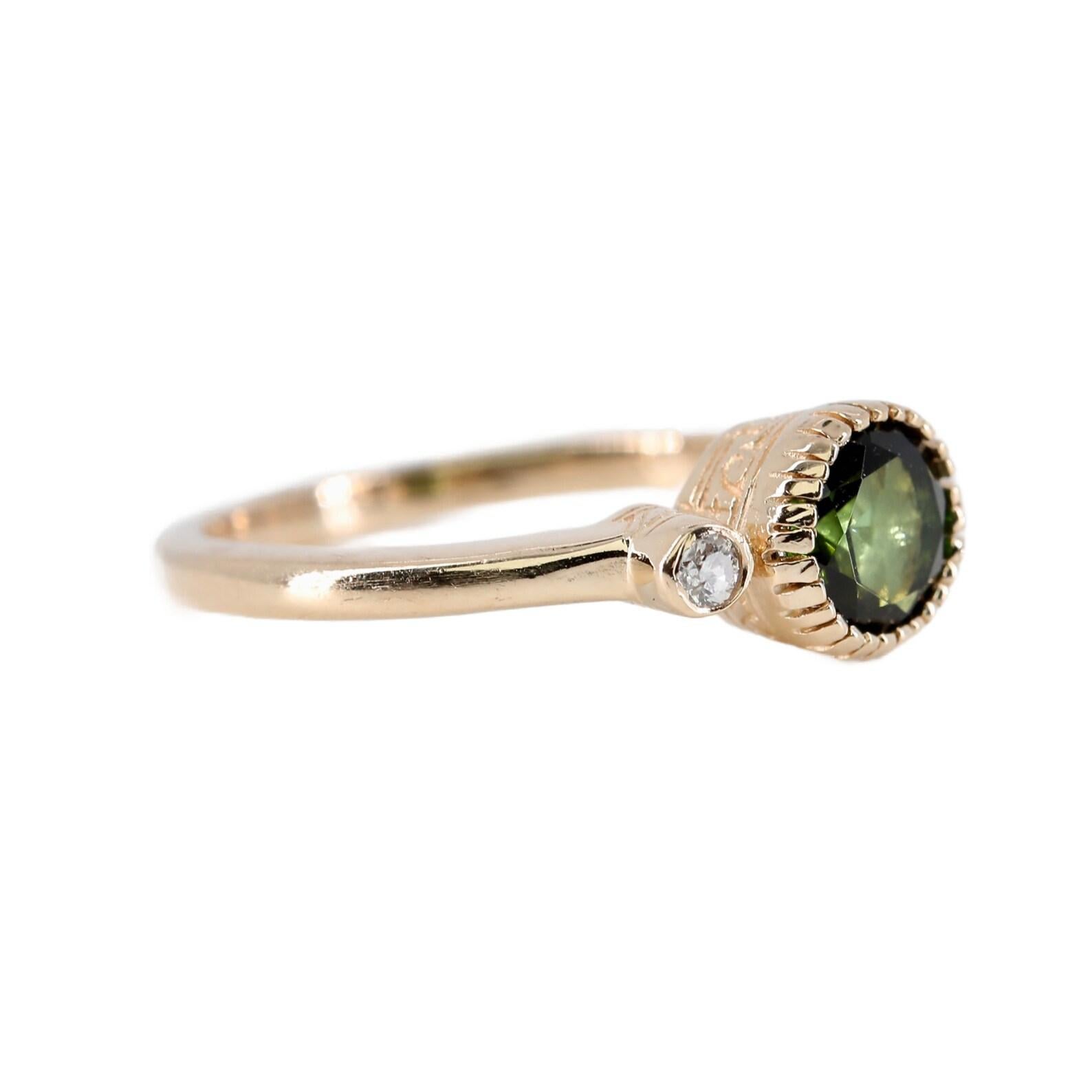 A vintage three stone green tourmaline, and diamond ring. Crafted in 14 karat yellow gold, this ring is centered by a 1.00 carat natural green tourmaline. Framing the tourmaline are two diamonds of 0.08 carats. The mounting is completed by miligrain