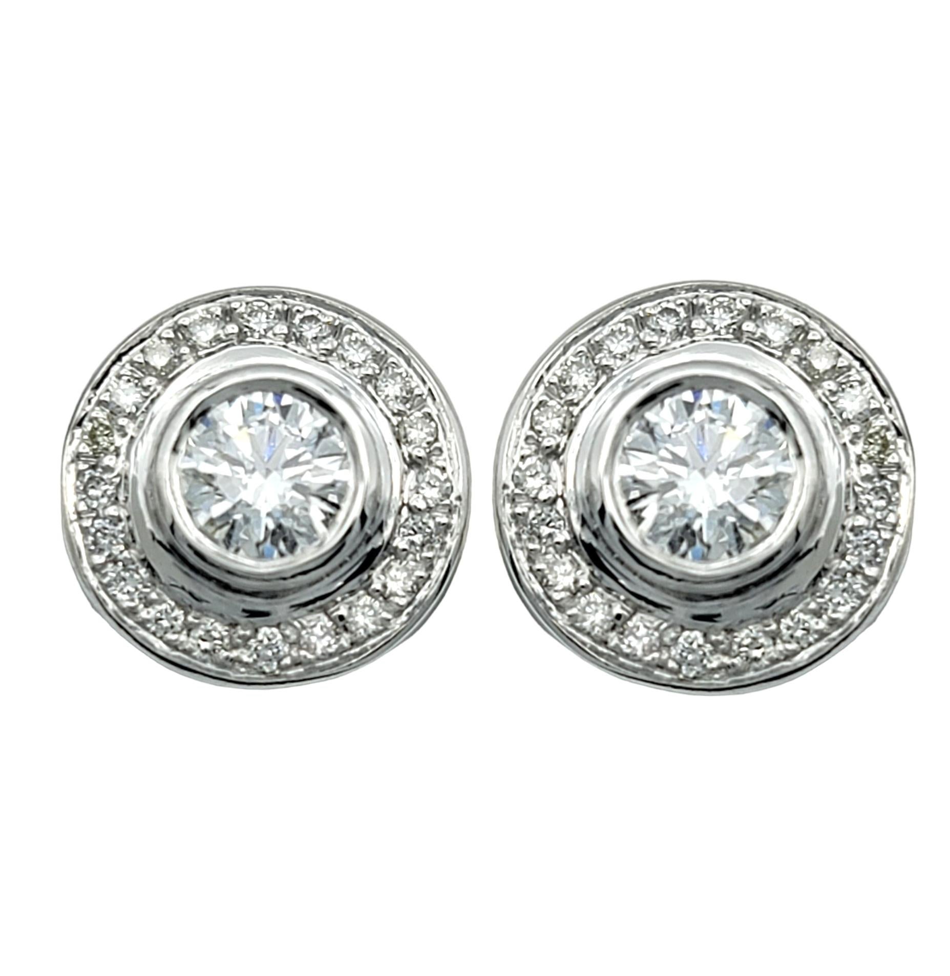 This gorgeous pair of diamond earrings is elegantly crafted in 14 karat white gold. The centerpiece of each earring is a brilliant round diamond, securely encased in a sleek bezel setting that highlights its radiance.

Encircling the central diamond