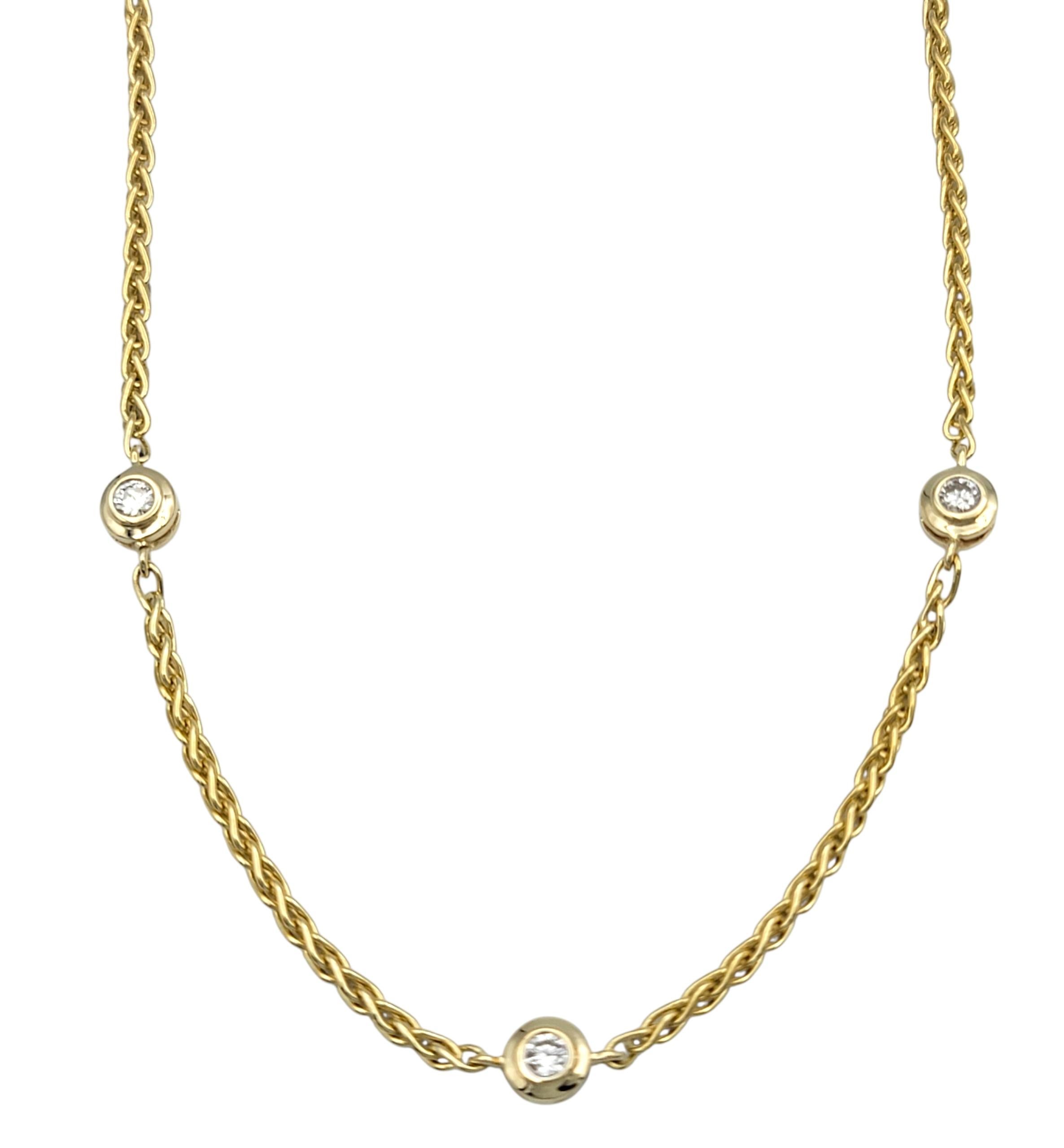 This timeless necklace showcases a delicate line of bezel-set round brilliant cut diamonds, each carefully placed along a refined 18 karat yellow gold wheat chain. The design embodies understated elegance, making it perfect for layering or wearing