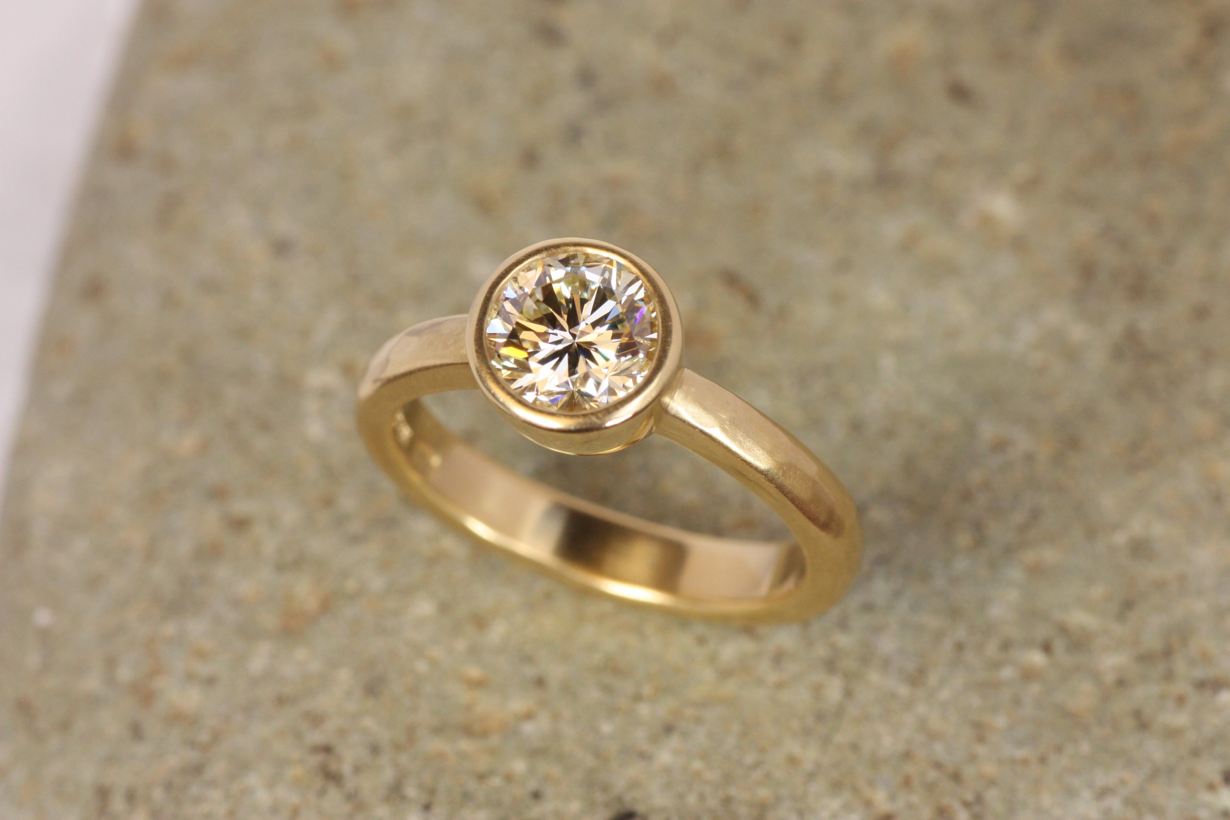 This one-of-a-kind solitaire engagement ring combines an earthy, ancient aesthetic with classic design. A 1.35ct natural round diamond with warm golden tones and exceptional clarity is bezel-set in solid 22K yellow gold. The hammered finish on the