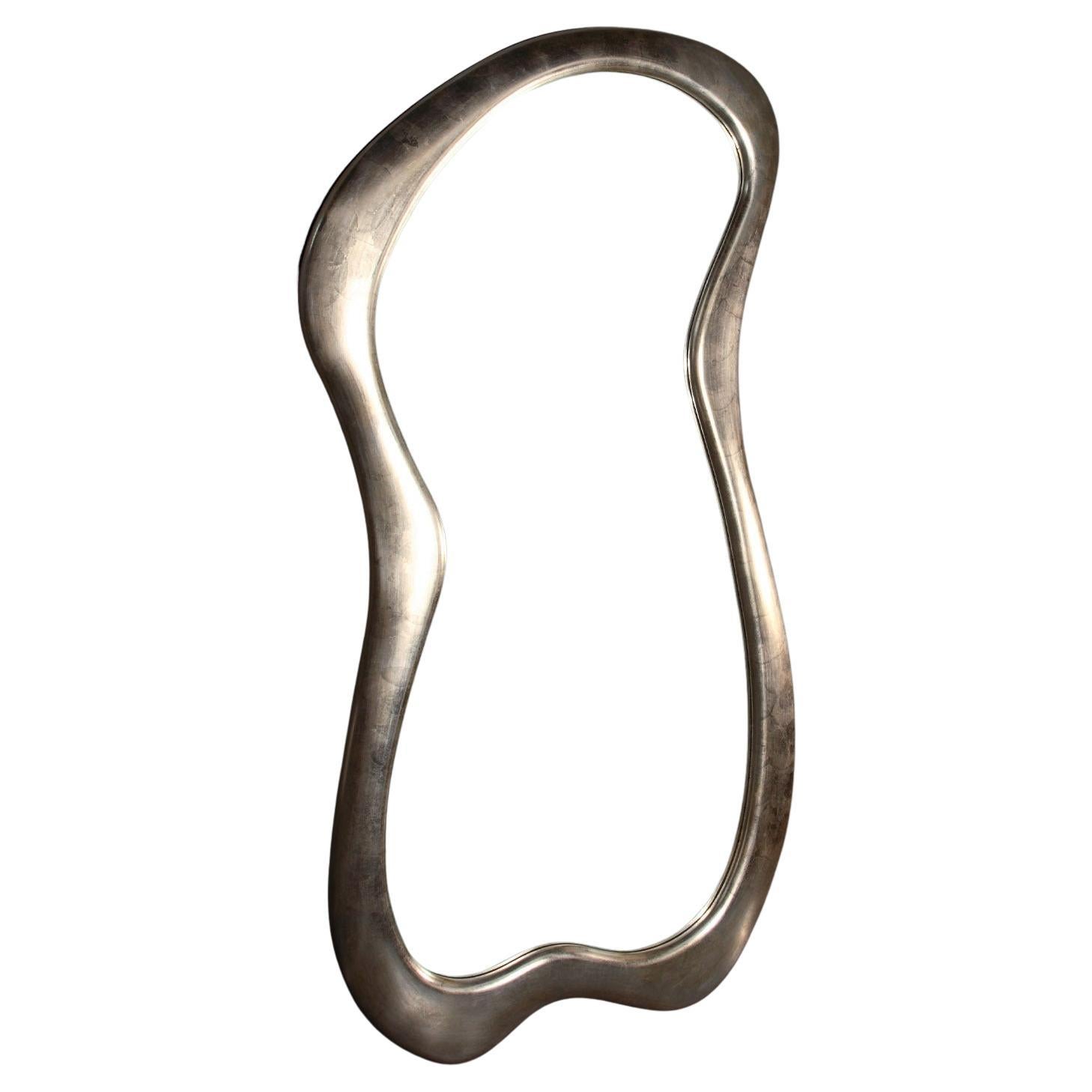 Progettato pensando allo stile Avant Garde, questo specchio da parete è un esercizio di linee fluide e finiture raffinate che gli conferiscono un'eleganza senza tempo. La preziosa foglia d'argento ricopre la sinuosa cornice, per una lucentezza che