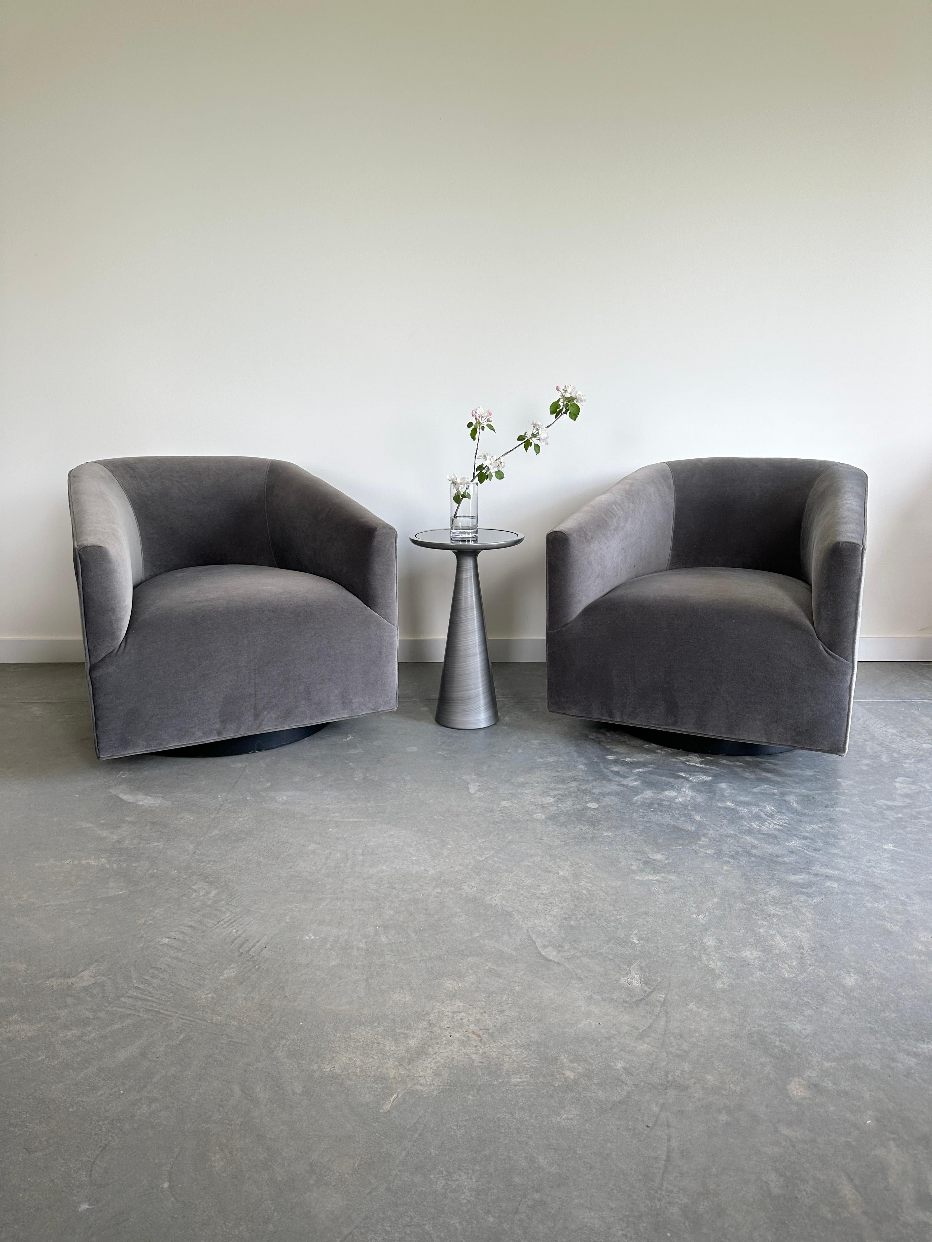 The Bianca Swivel Chair is a cozy and chic chair that can swivel and recline for your comfort. It features a barrel-back design with a clean silhouette on a round wood base. The chair is upholstered in a soft and luxurious grey velvet fabric with a