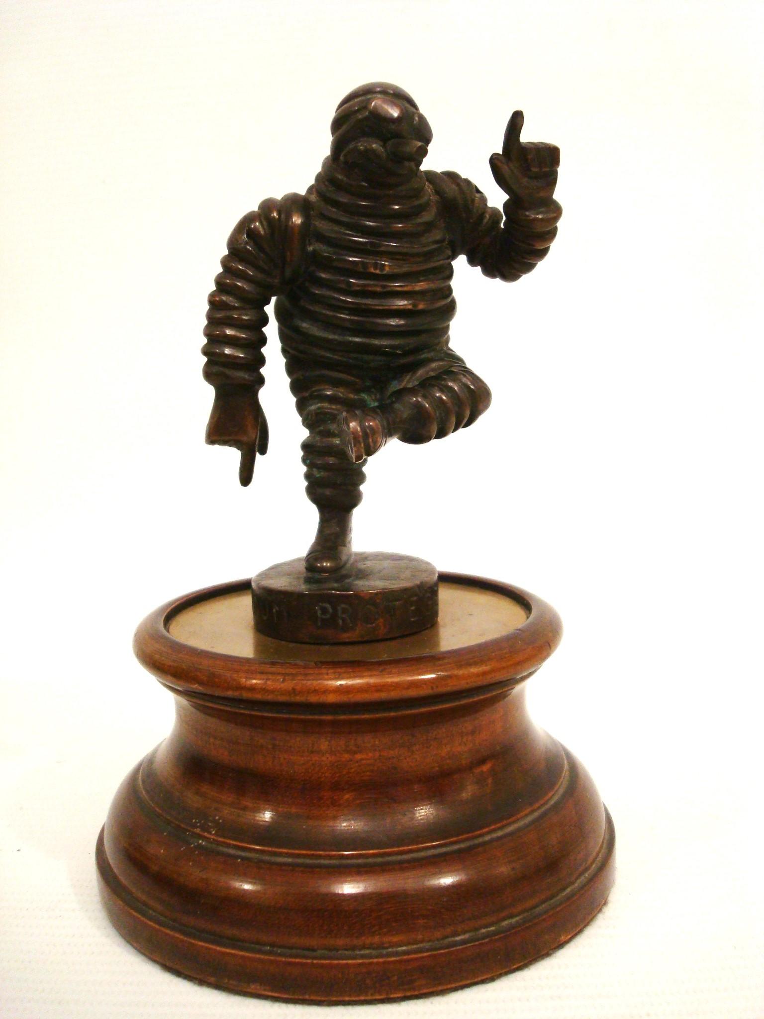 Dies ist eine sehr sammelwürdige Bibendum Michelin Man Bronze Auto Maskottchen, Hood Ornament, Mascotte voiture.
Das Michelin-Männchen, auch bekannt als Bibendum, ist ungefähr 4 Zoll groß und hebt freudig den Arm, während es fröhlich sein Bein