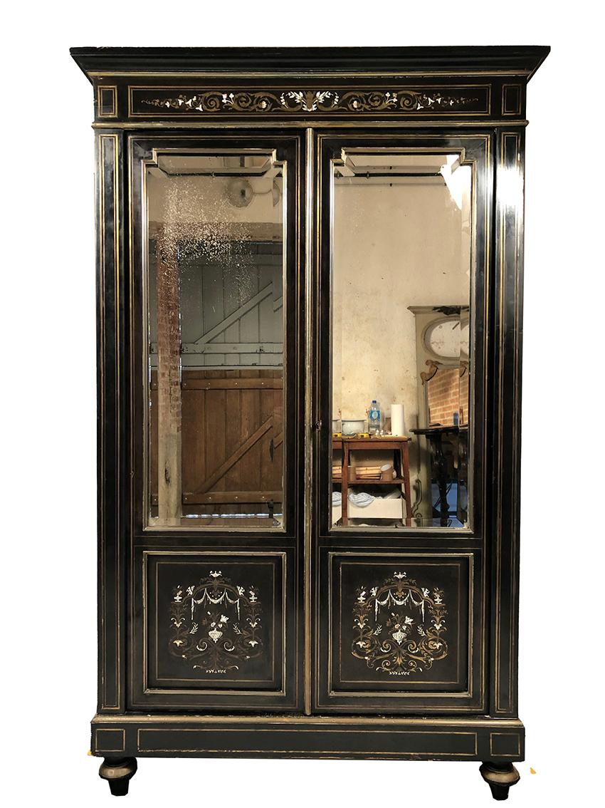 Bibliothèque Napoléon III, bois noirci marqueté de laiton, d’ivoire et de nacre.
Elle ouvre à deux portes à fond de miroir biseauté (tain piqué à plusieurs endroits)
sur quatre étagères,
intérieur en placage d’acajou
Ferme à clé.
Elle repose sur
