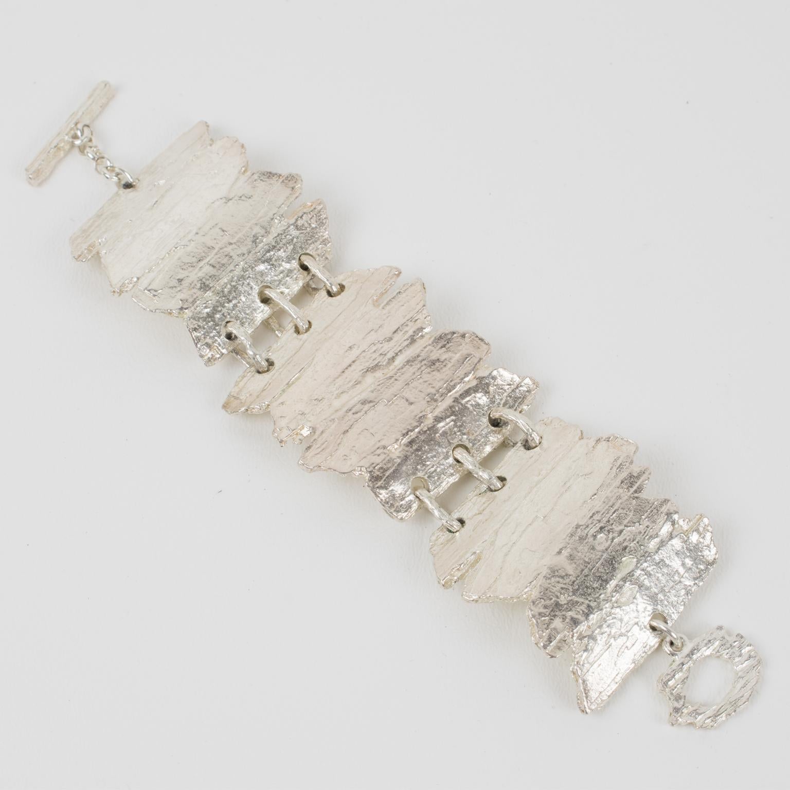 This stunning modernist silver plate link bracelet by Nelly Biche de Bere, Paris, boasts a chunky oversized bangle with a brutalist carved and hand-made feel design. The design features driftwood with a textured pattern. The three elements are