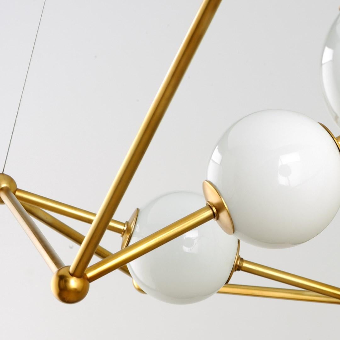Martyn Lawrence Bullard for Corbett Lighting
A bright example of angular modern design. 
The Bickley Chandelier pairs a rhomboid Solid Brass frame with a perfectly round sphere of light-diffusing White Opal Glass. 
The Vintage Brass finish and round