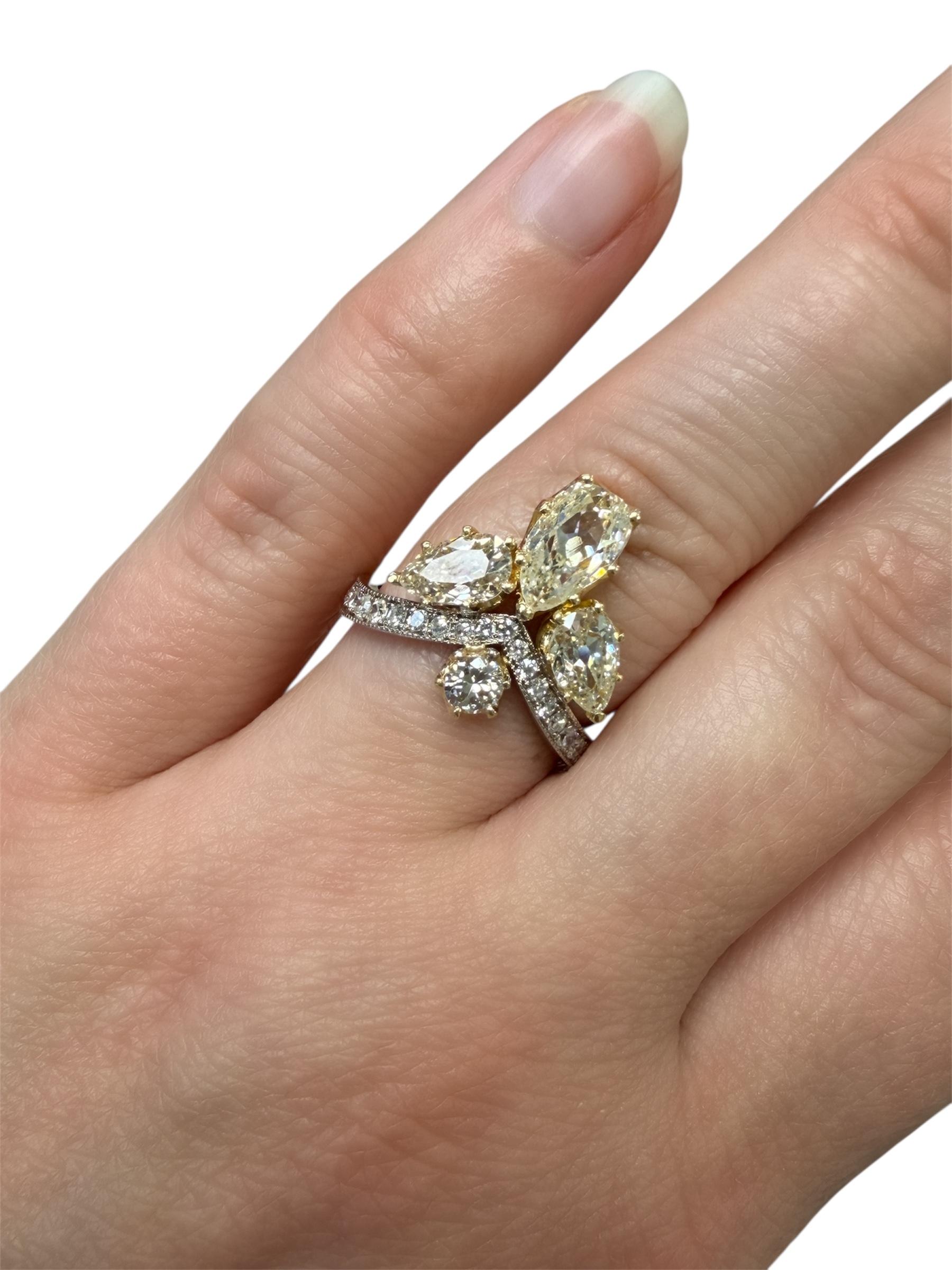 Cette magnifique bague à la fleur de lys est ornée de trois diamants anciens en forme de poire de couleur chaude, d'un diamant ancien de taille européenne et d'un anneau serti de diamants simples d'un blanc éclatant. Cette bague extraordinaire