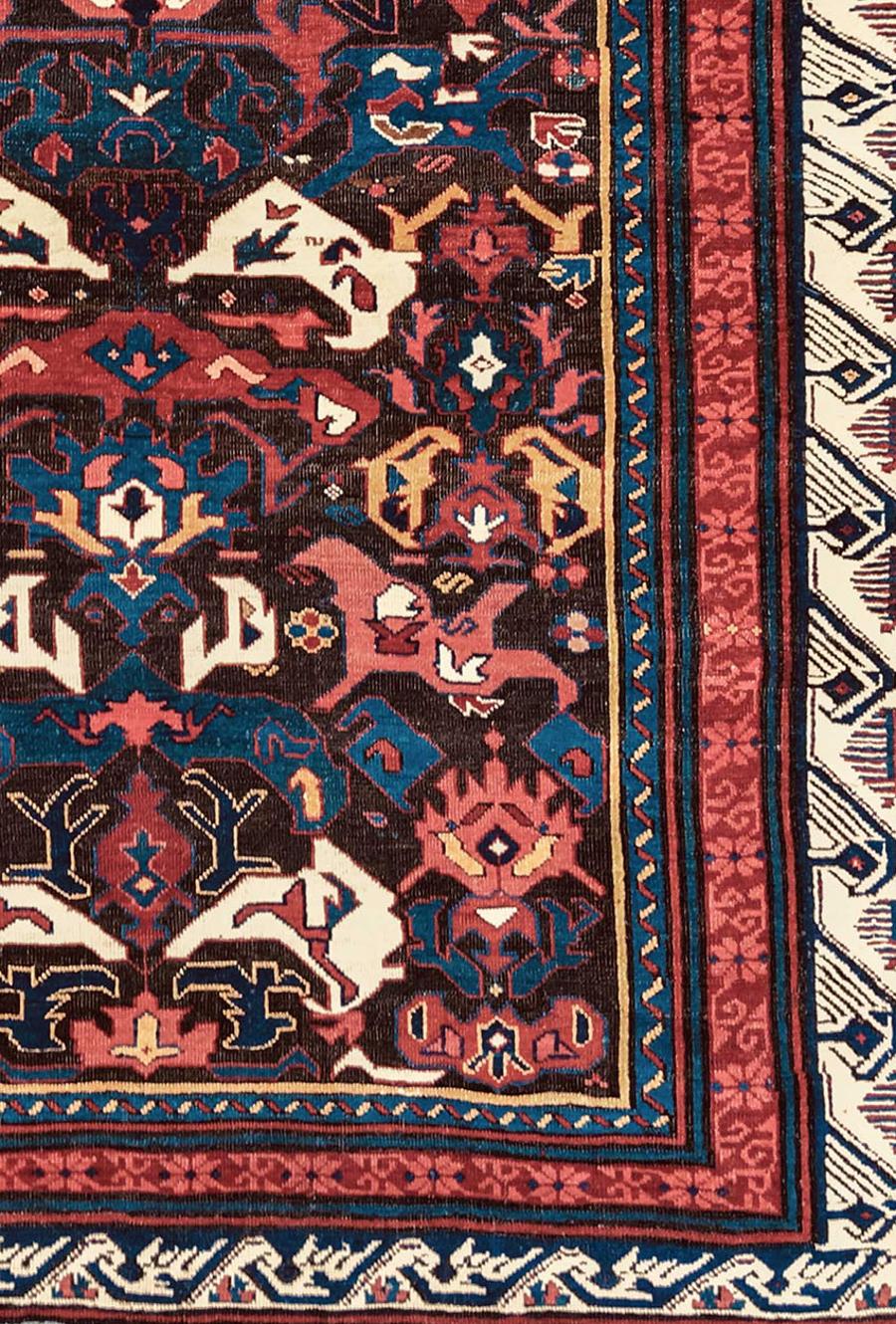 The deep brown oxidized field of this Bidjov Kuba rug from the southeast Caucasus provides the perfect canvas for the various colorful abstract vegetal elements radiating against it. Together these forms combine to create a stylized rendition of the