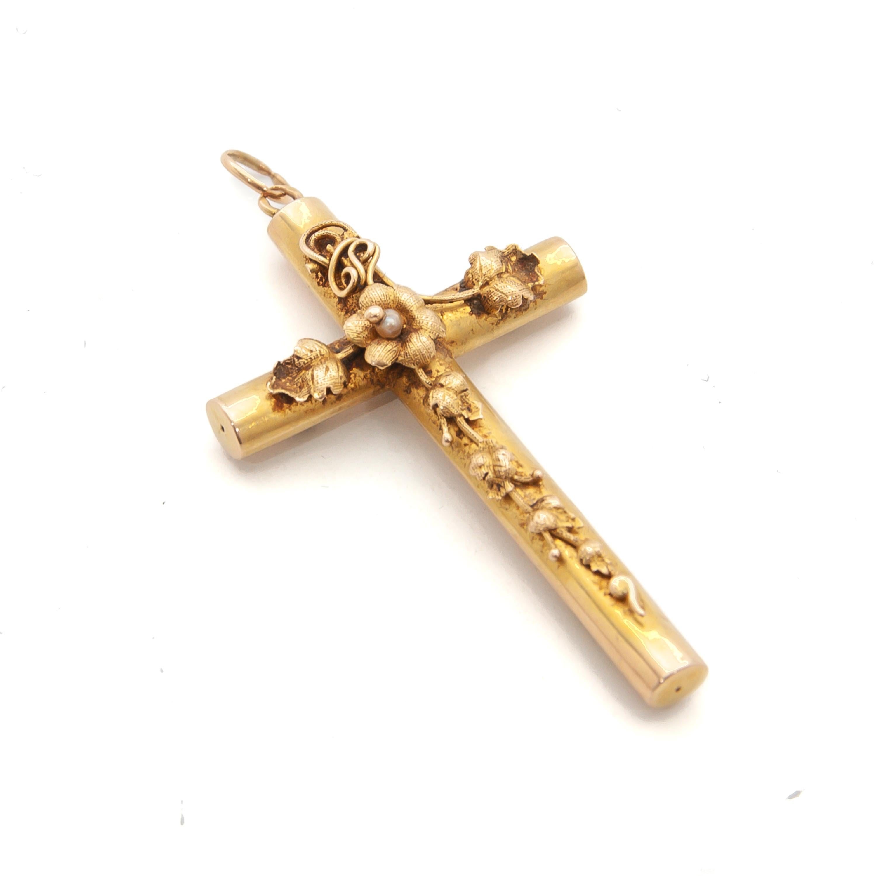 An antique Victorian cross pendant crafted in 14 karat yellow gold created with a chased ornamental decor. The design of the cross is embellished with tendril and leaf motifs from top to bottom. In the center of the crossed bars a cannetille flower