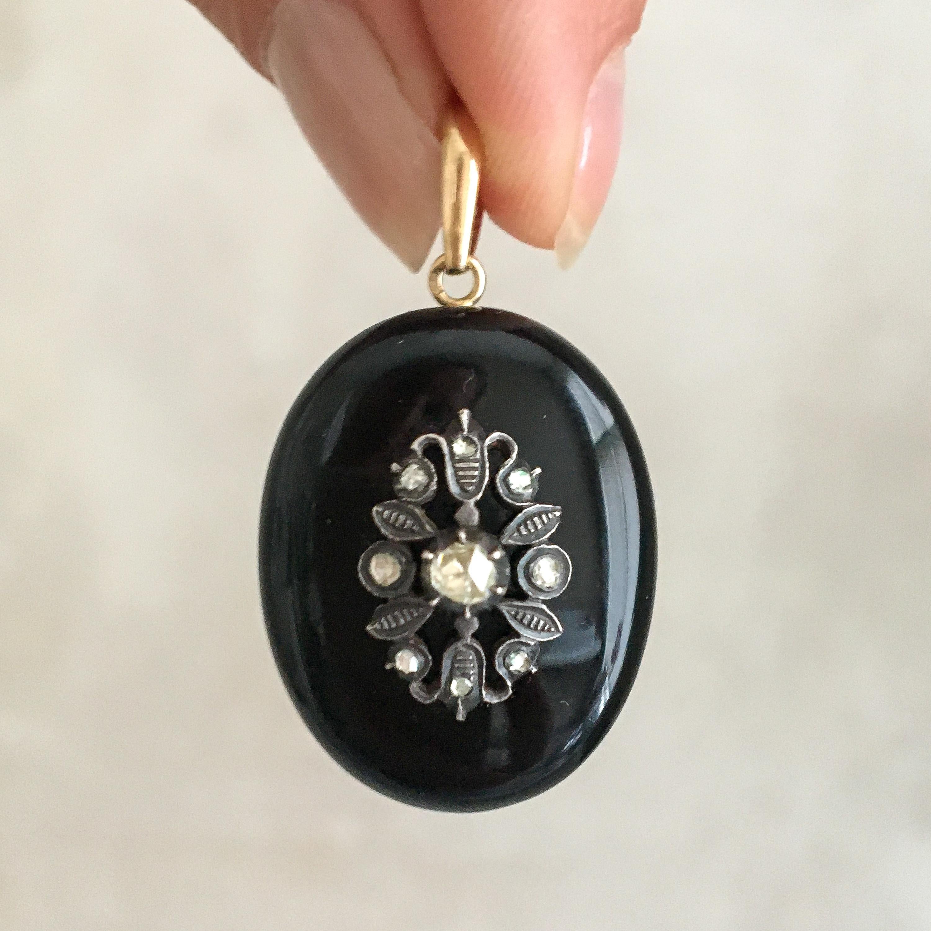 An antique Late Victorian, 1880-1890, diamond and onyx locket pendant. In the center, the onyx stone is decorated with a silver floral decor set with rose cut diamonds. The pendant is oval-shaped and is being held by a 14 karat gold bail. The onyx