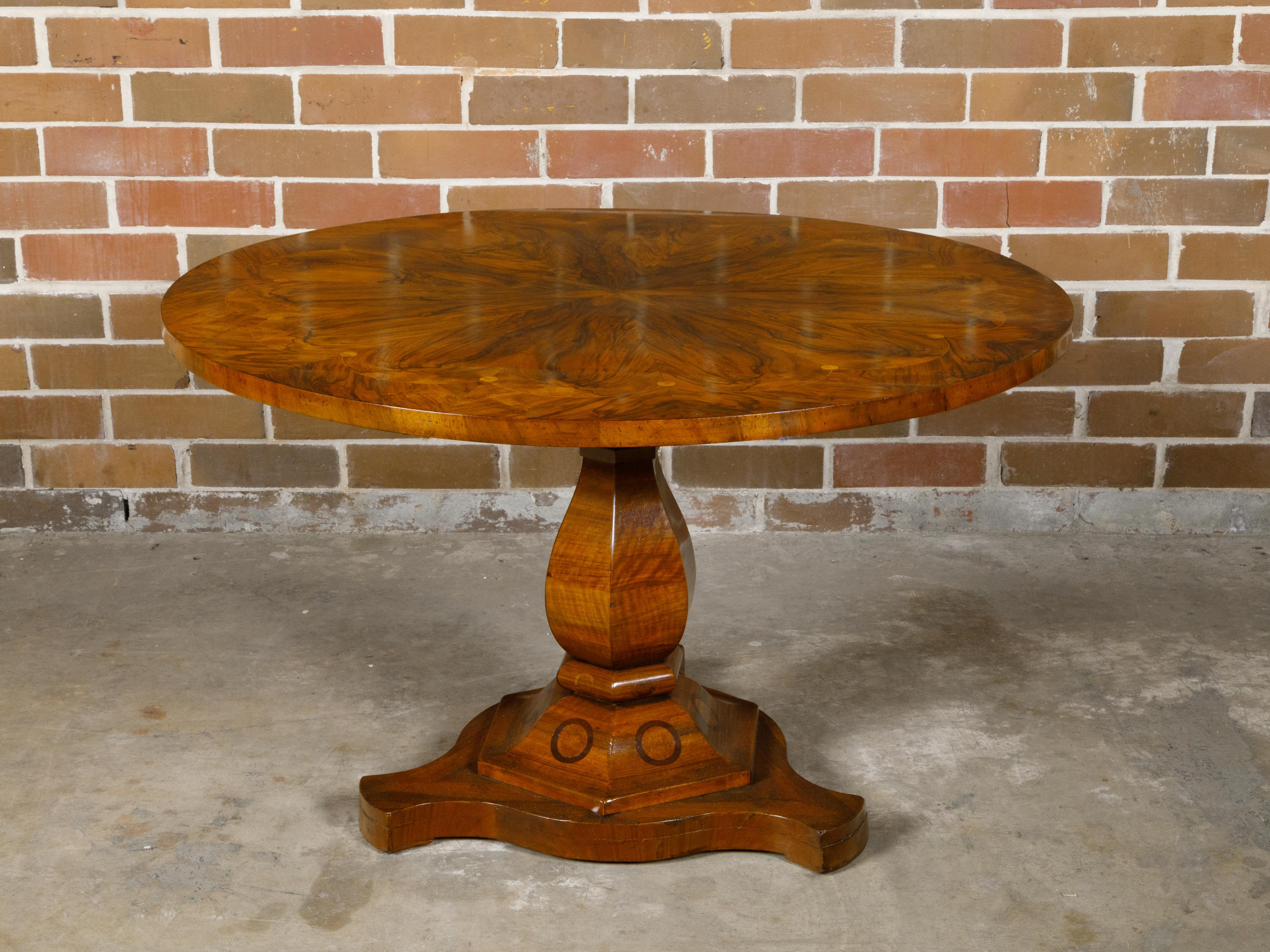 A Biedermeier period table from the 19th century with flame walnut circular top adorned with exquisite radiating motif and raised on pedestal base. This exquisite Biedermeier period table, dating back to the 19th century, showcases the era's refined